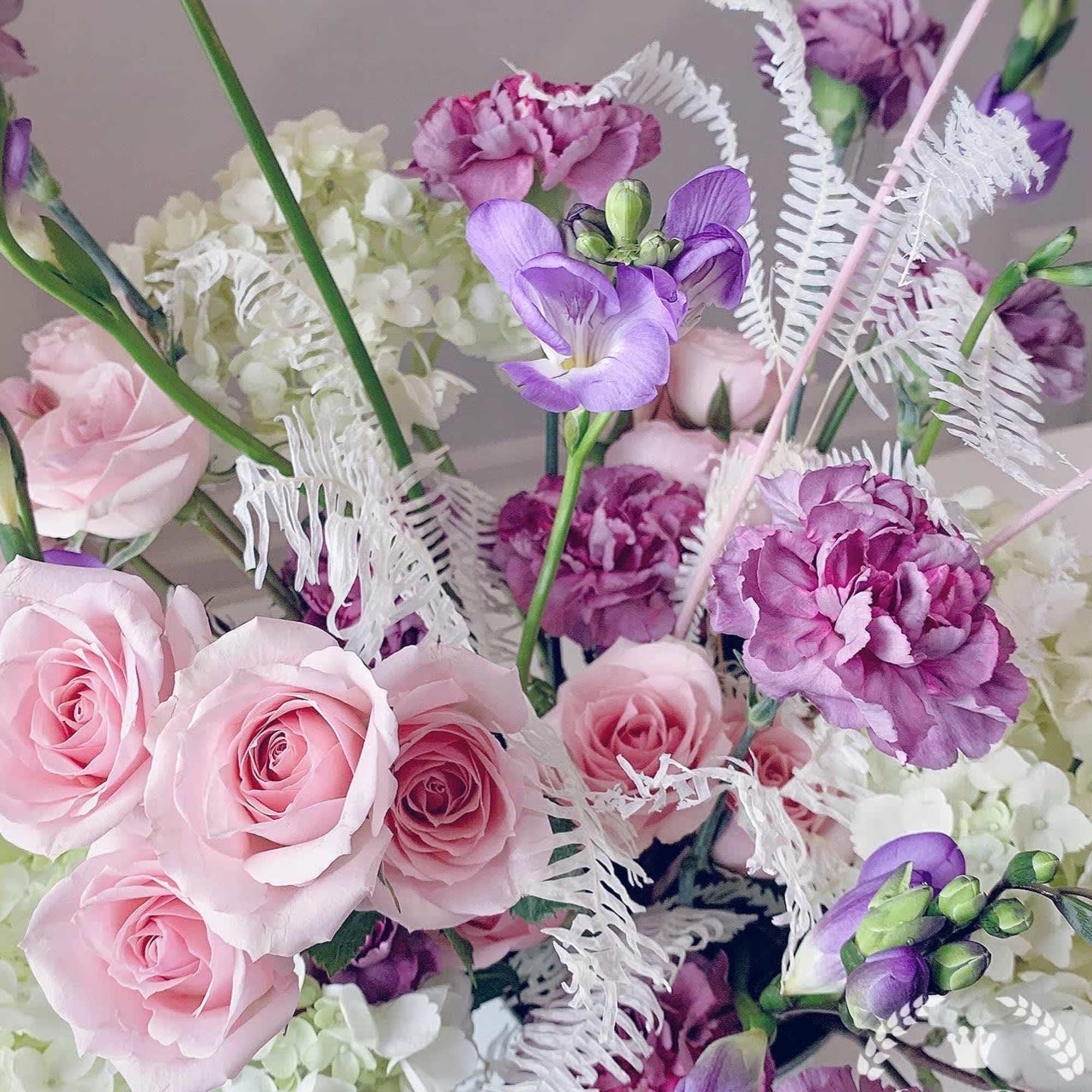 Pink roses and purple flowers arranged with white filler blooms.