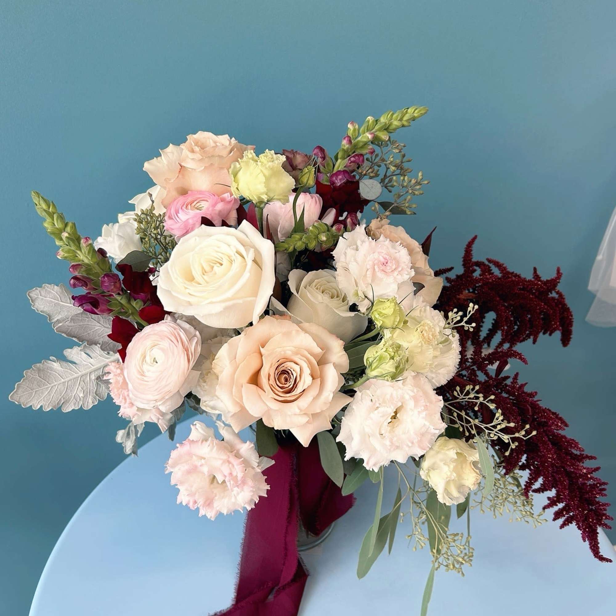 Mixed bouquet of roses, ranunculus, and lisianthus in a vase with burgundy ribbon