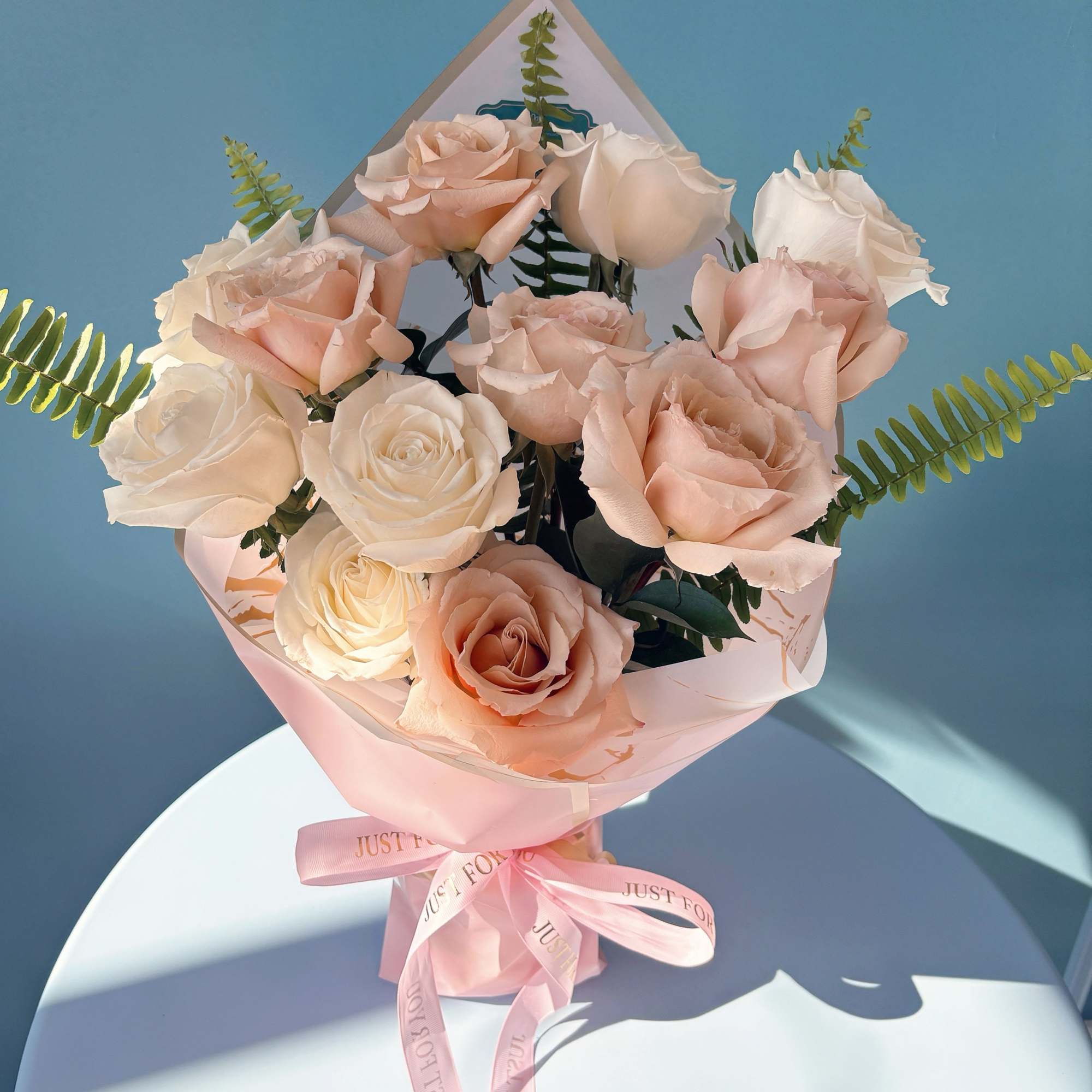 Bouquet of pale pink and white roses wrapped in pink paper with a ribbon