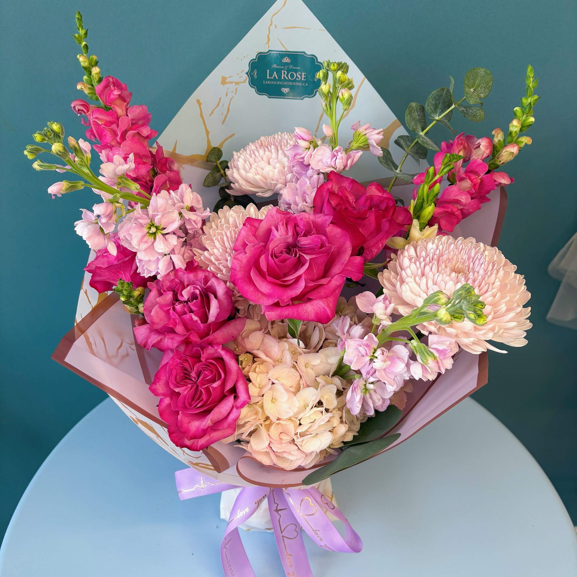 Pink roses and pale chrysanthemums in a wrapped bouquet with a lavender ribbon