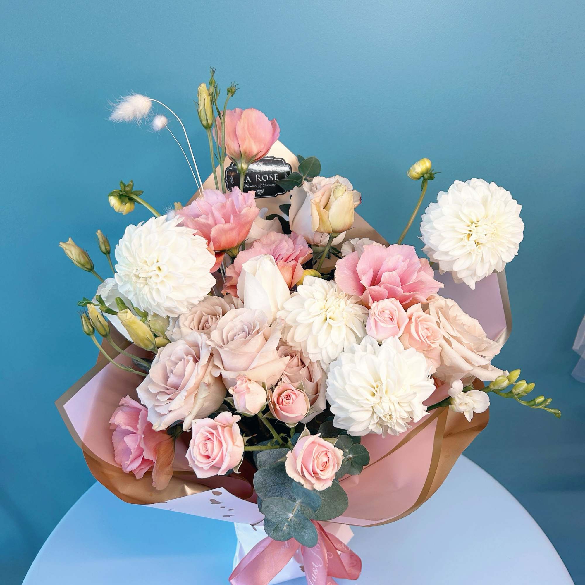 Pink and white bouquet of roses and dahlias wrapped in paper