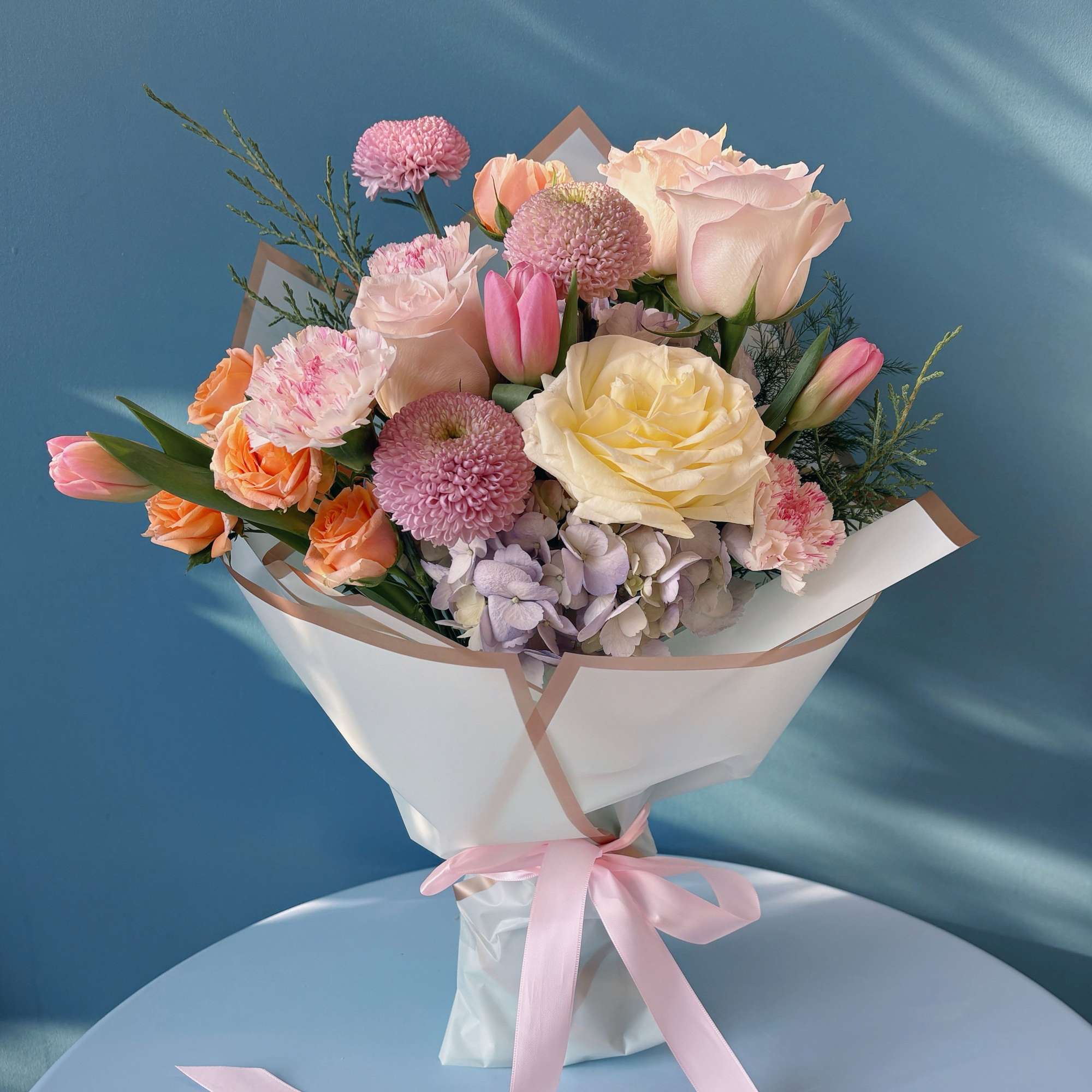 Pastel bouquet of roses, tulips, carnations, and chrysanthemums wrapped with a pink ribbon
