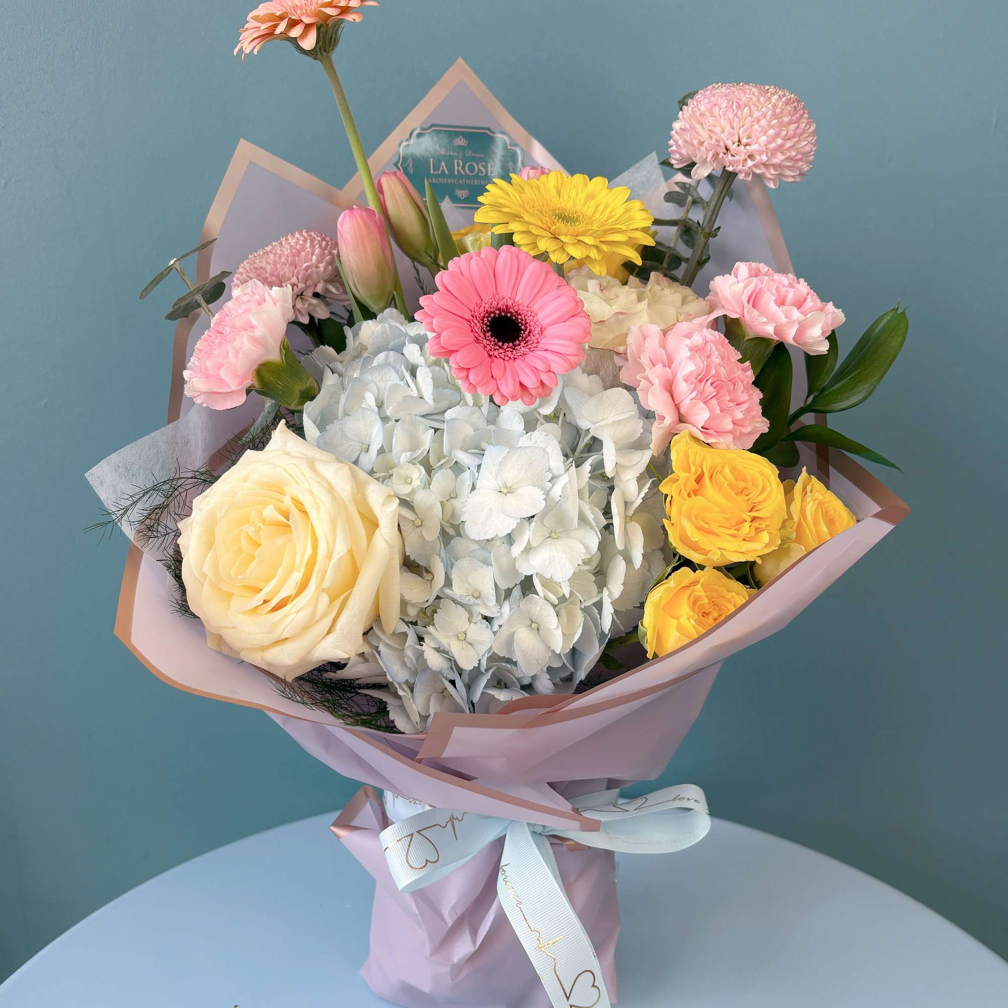 Mixed bouquet with pink, yellow, and white flowers wrapped in pink paper