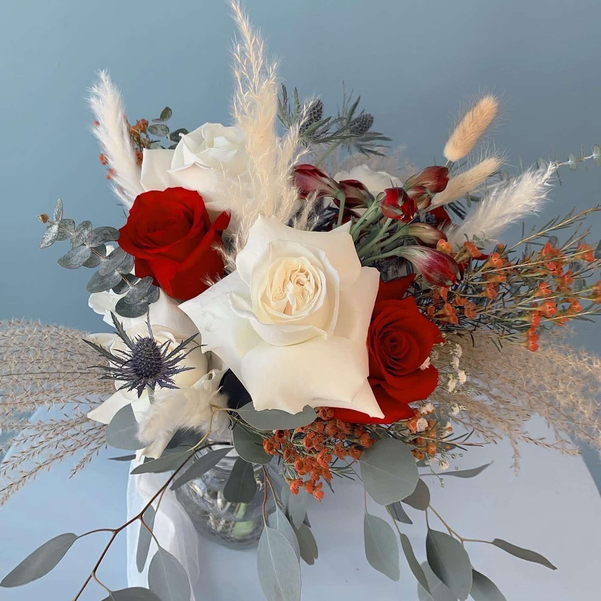 Bouquet of red and white roses with dried grasses in a glass vase