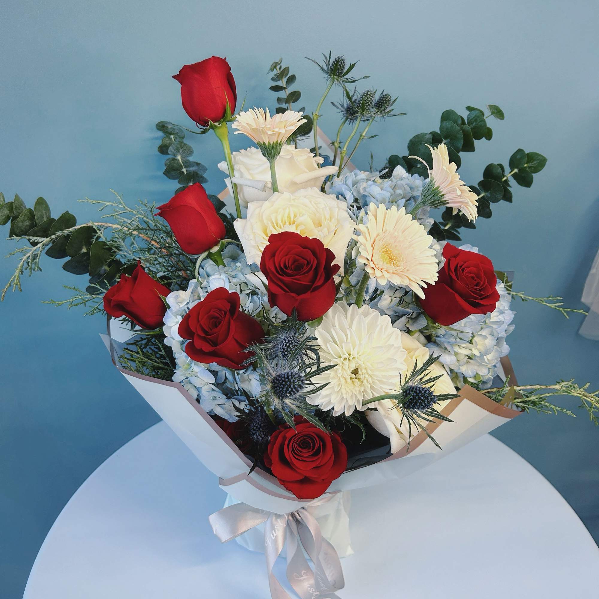 Bouquet of red roses, white blooms, and blue hydrangeas with a ribbon