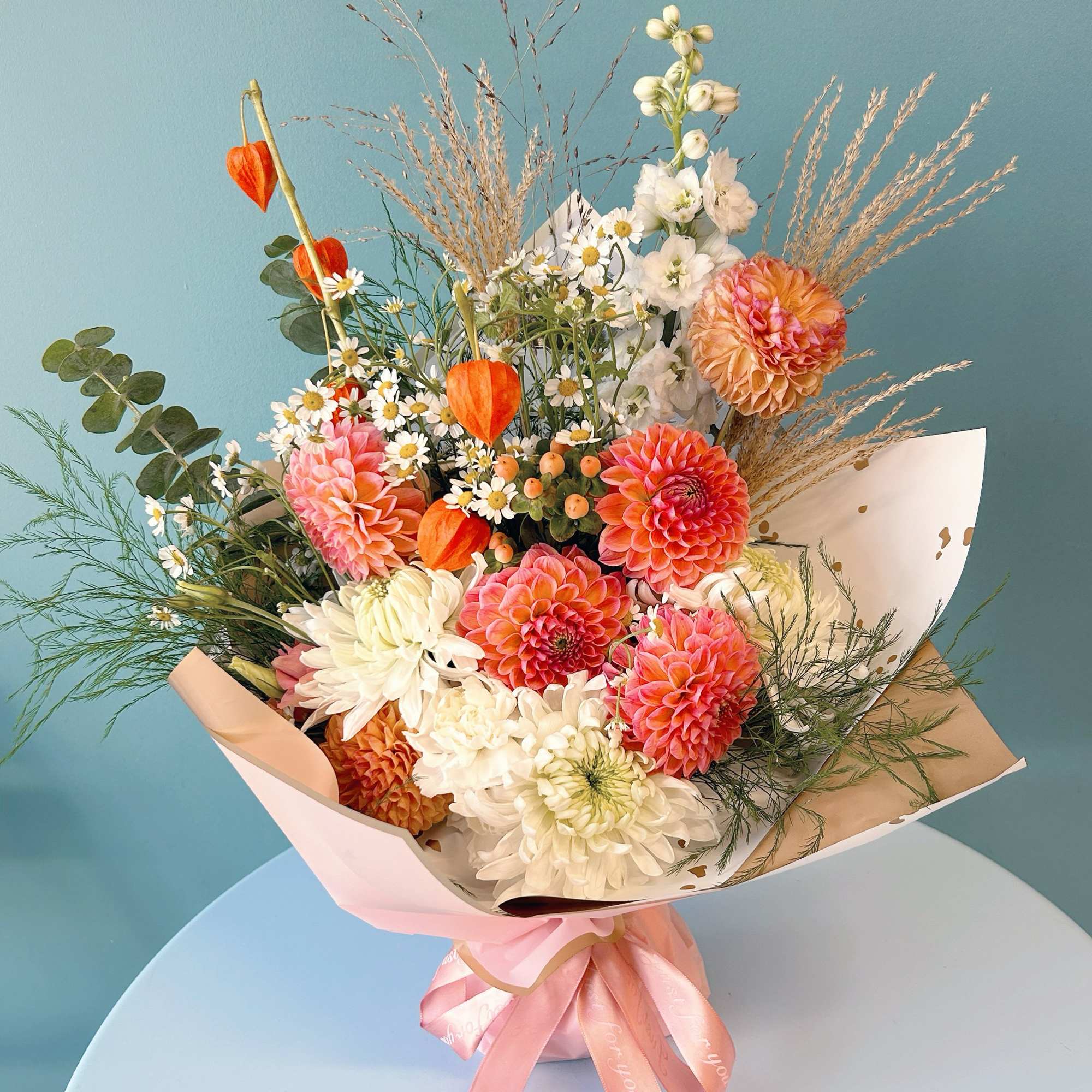 Mixed bouquet of pink, white, and orange flowers with a pink ribbon wrap