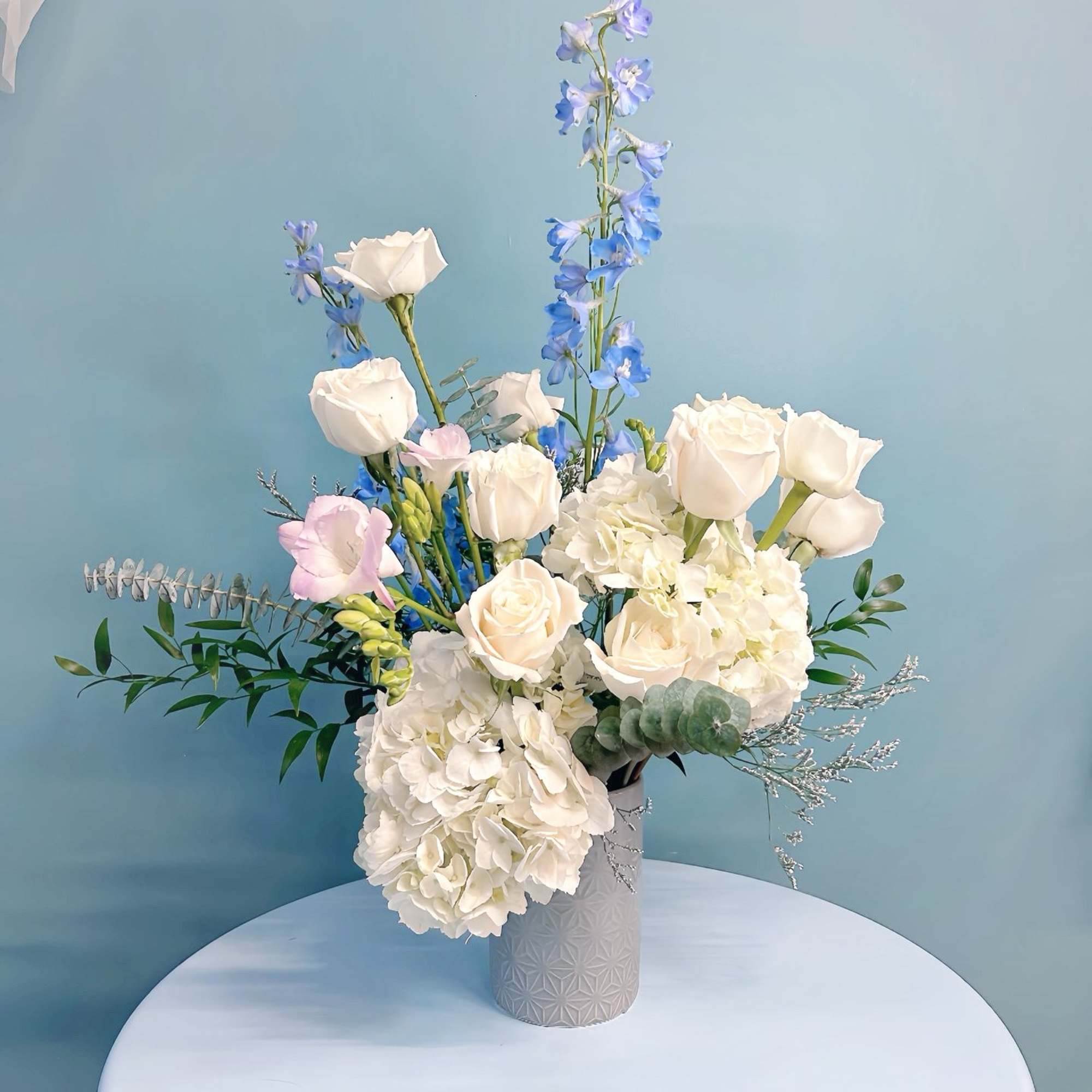 White roses and hydrangeas with blue delphinium in a gray vase