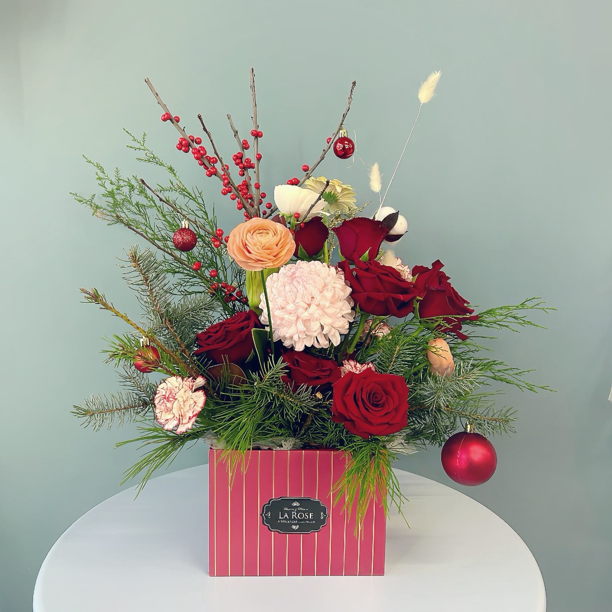 Holiday floral arrangement in a pink striped box with red roses and ornaments