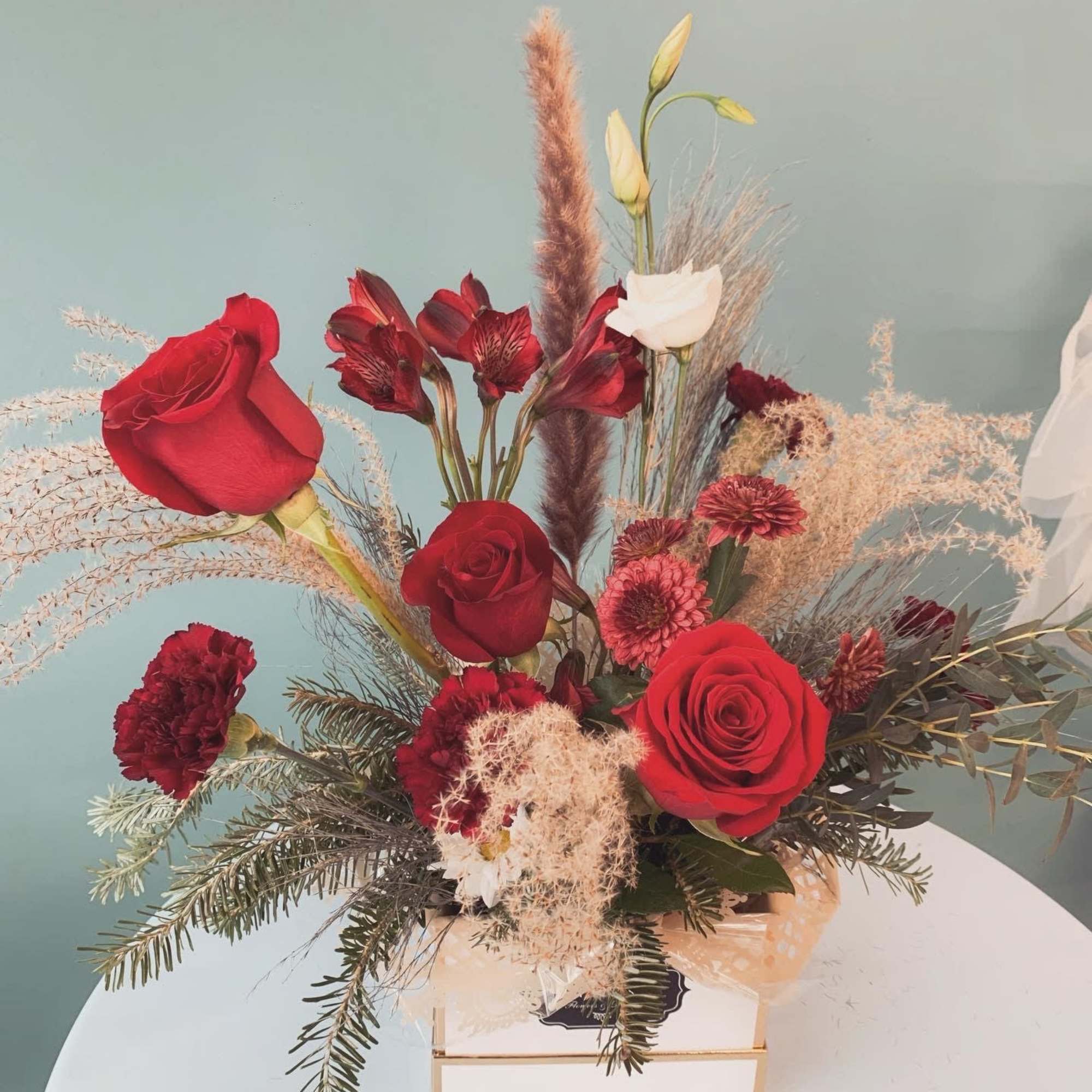 Red roses and burgundy flowers arranged in a box with dried grasses