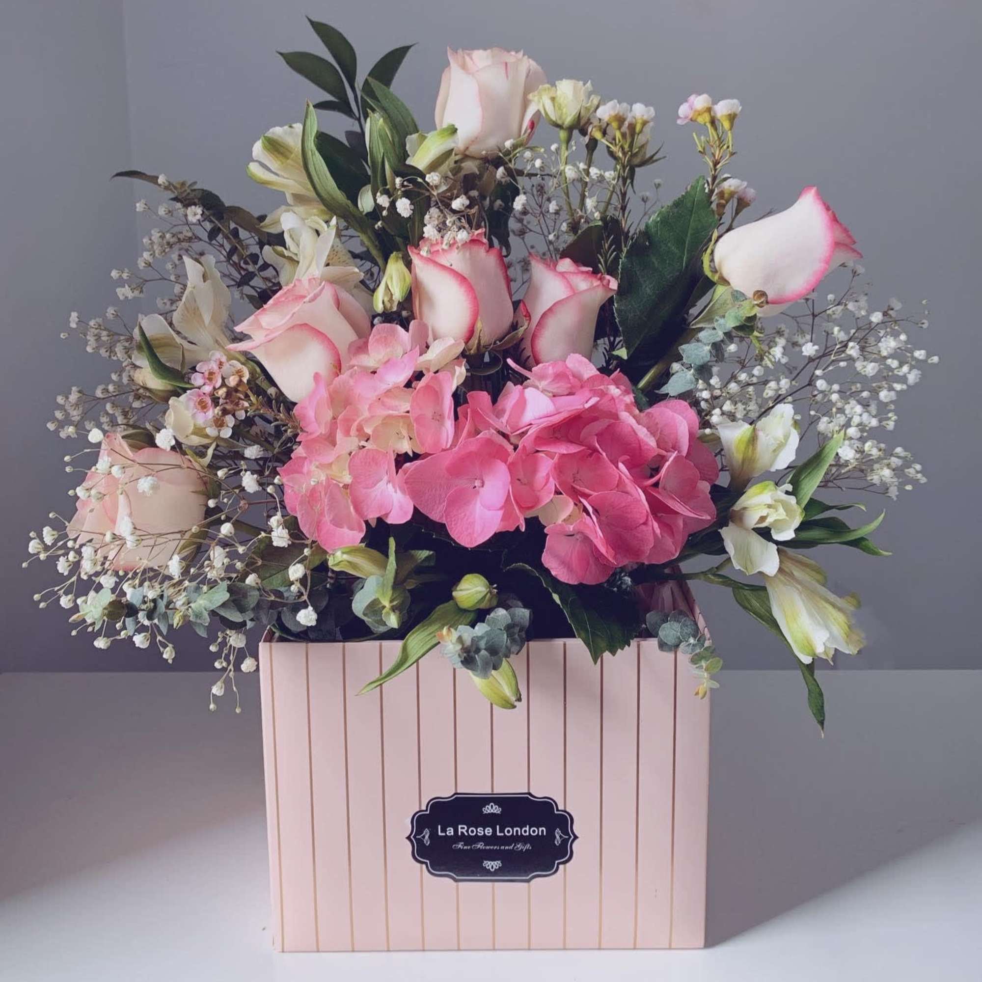 Pink and white floral arrangement in a striped pink box