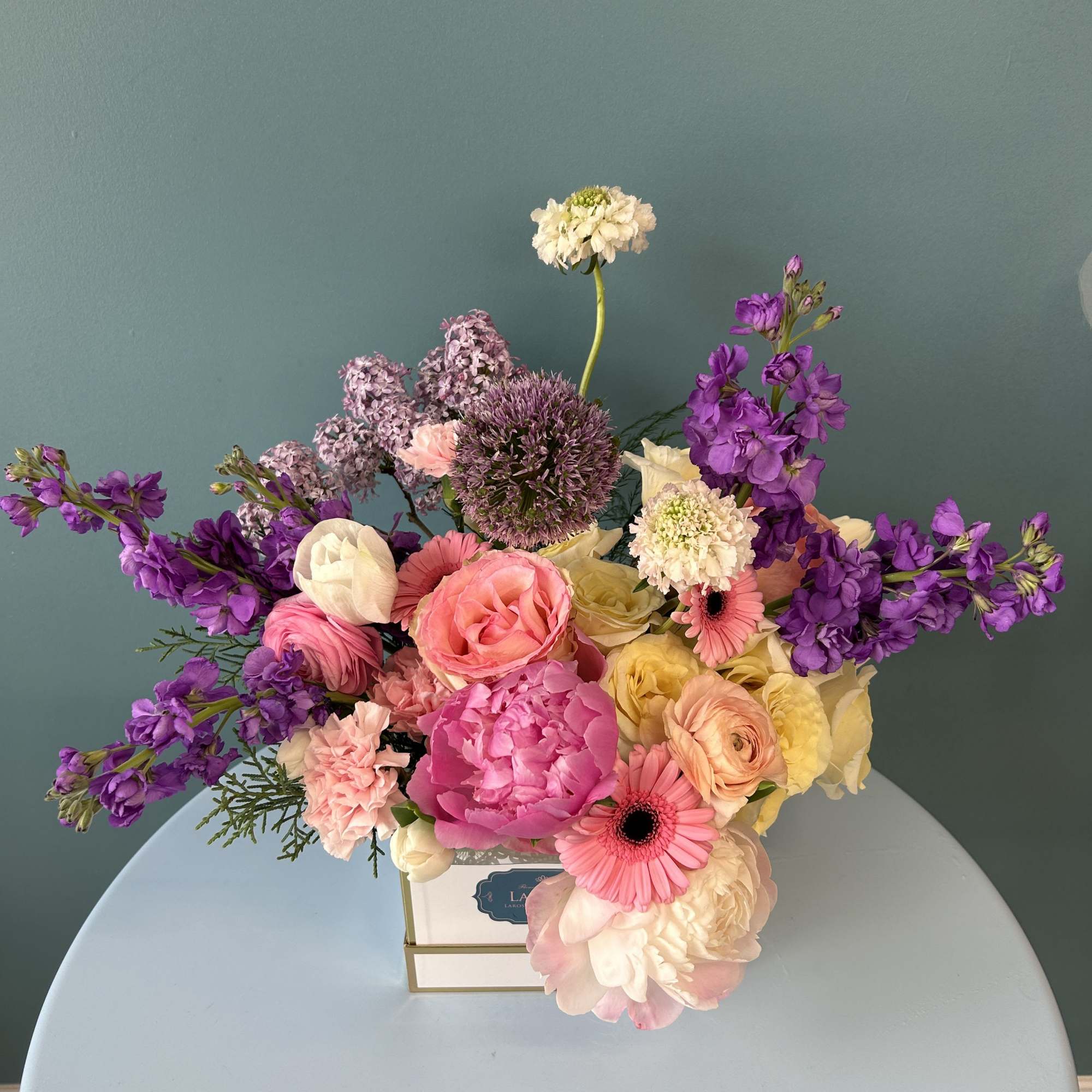 Mixed bouquet of pink, purple, and cream flowers in a square box