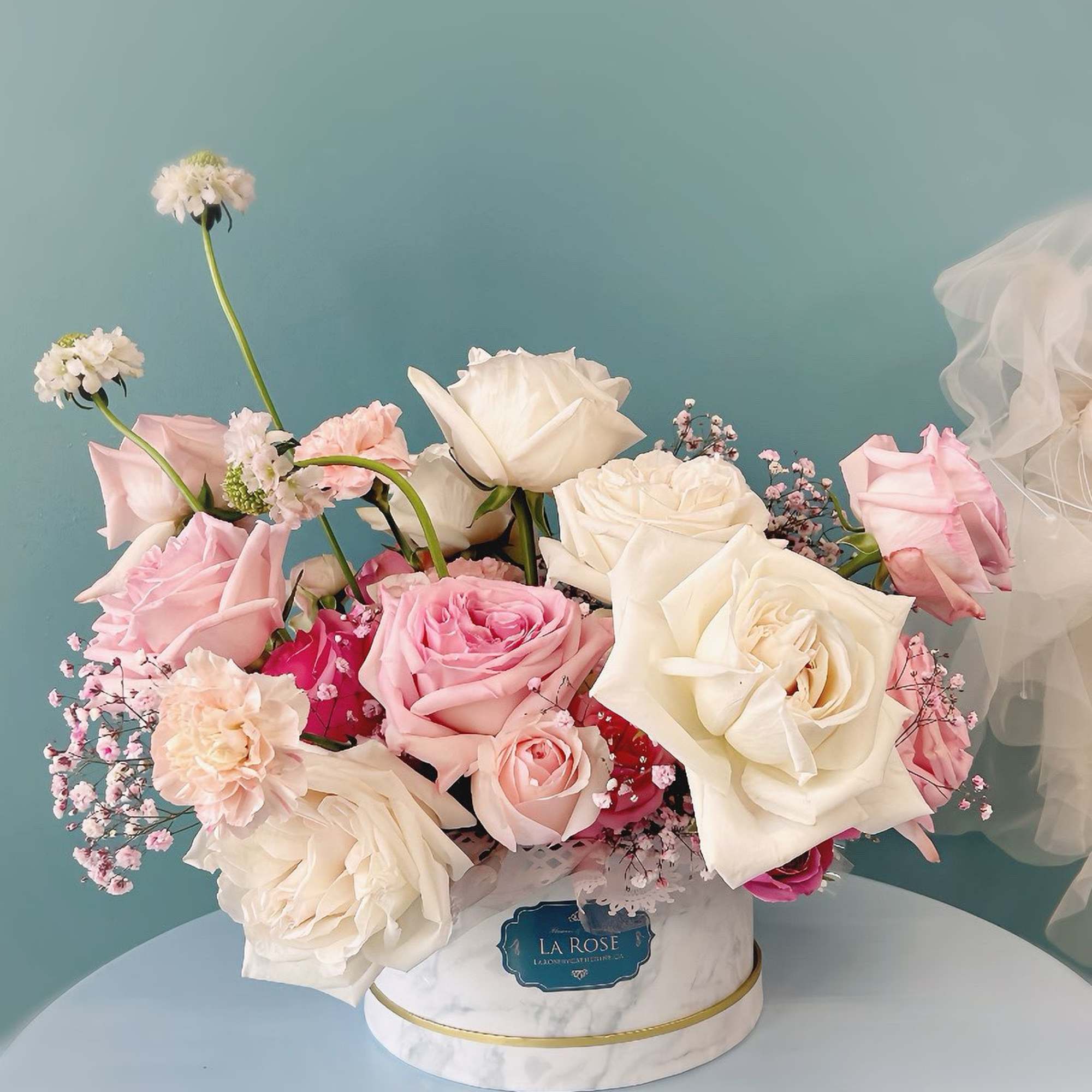 Pink and white roses arranged in a round marble-look box
