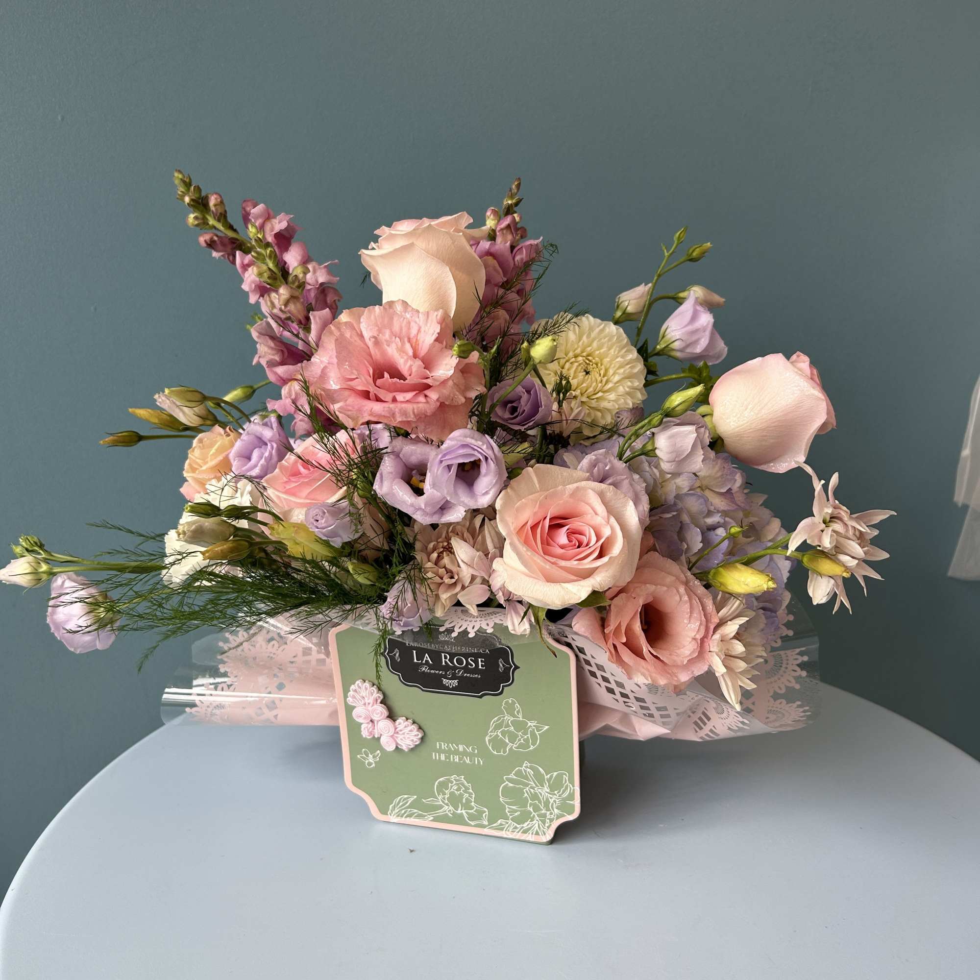 Pastel bouquet of roses, lisianthus, and snapdragons in decorative wrap