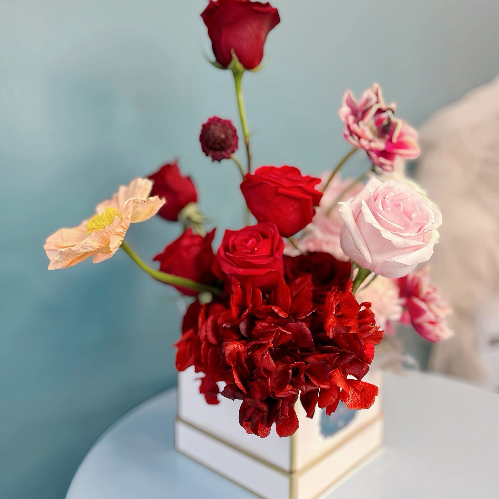 Mixed red and pink flowers arranged in a white square box