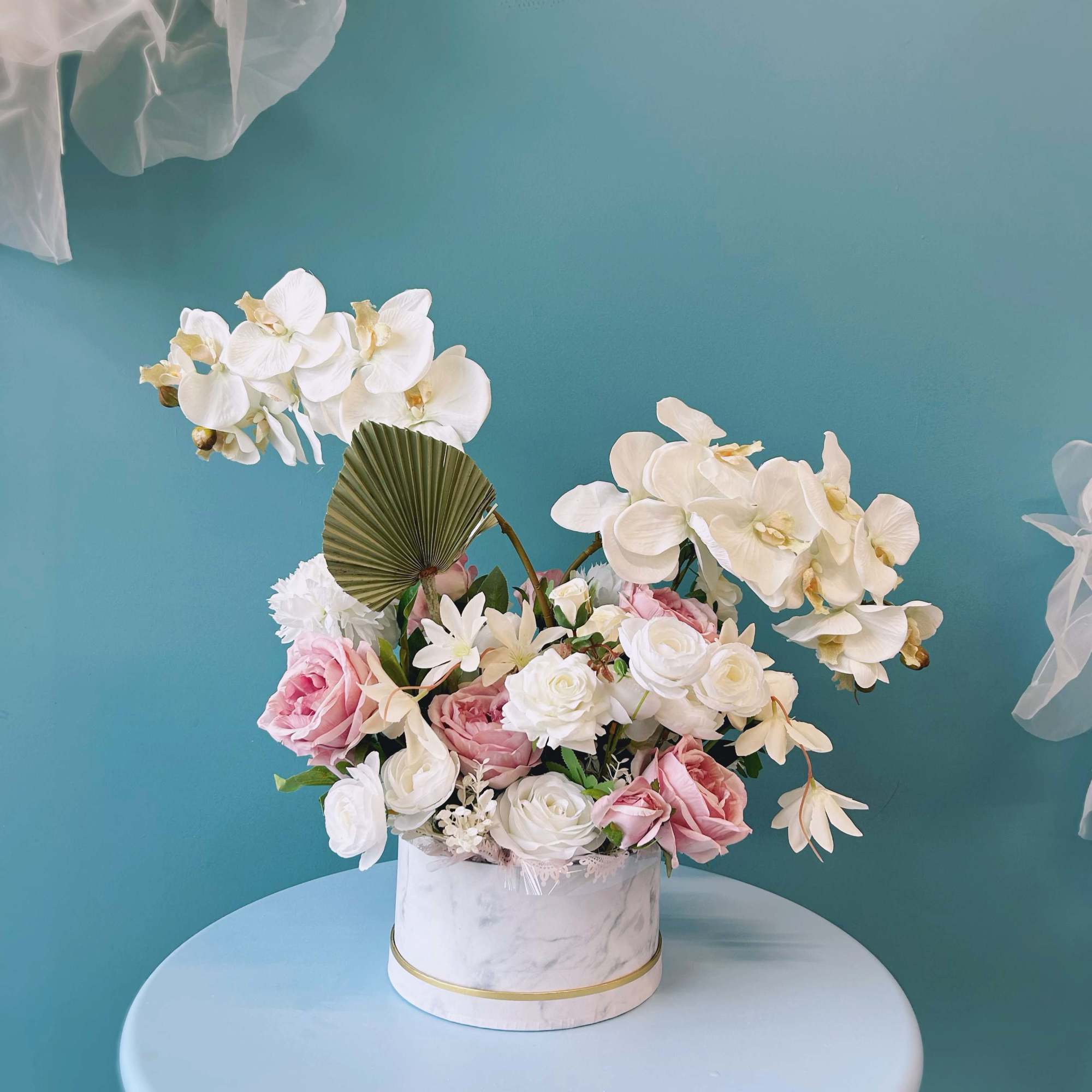 Pink and white floral arrangement in a round white box with orchids and roses
