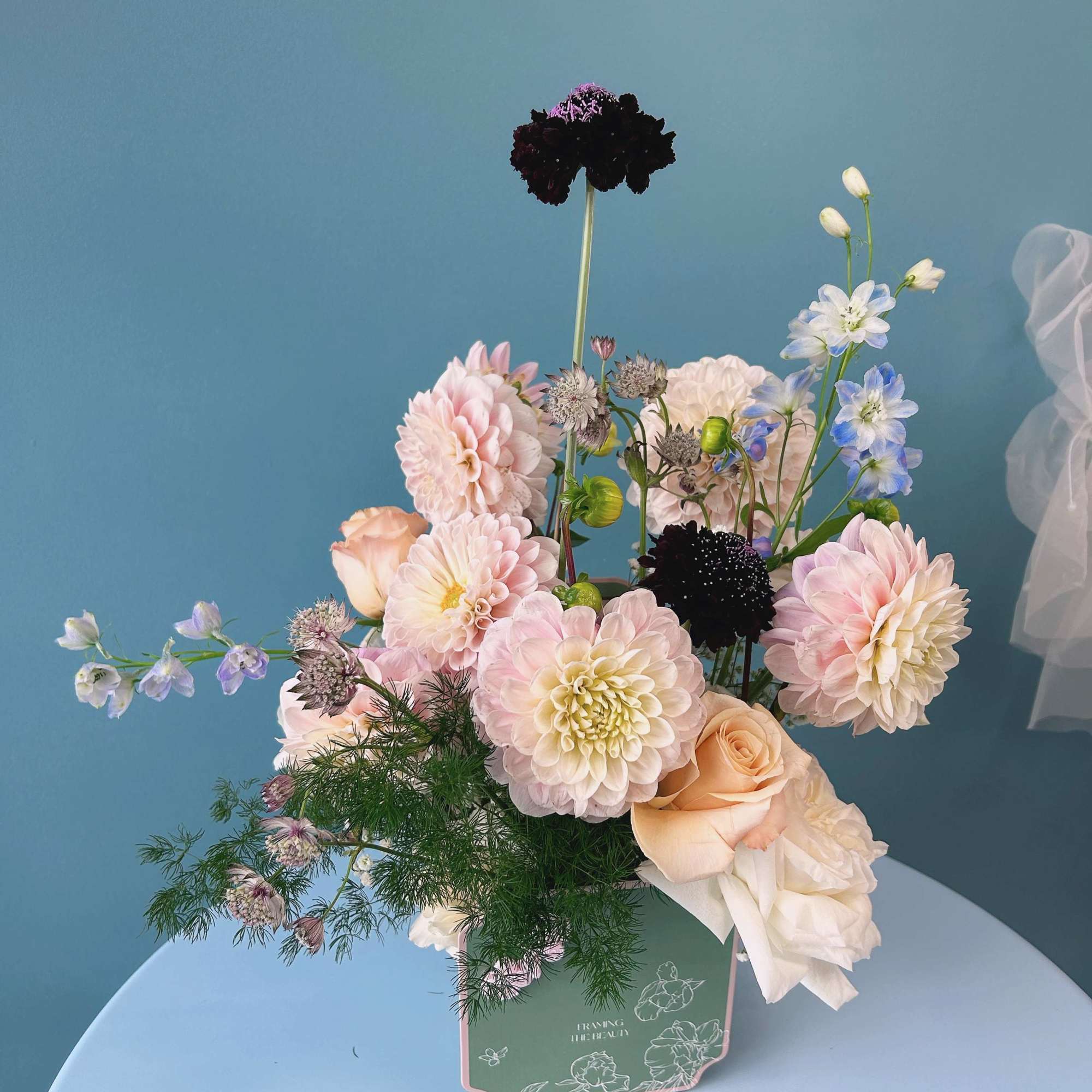 Pastel bouquet of dahlias, roses, and blue delphinium in a green box