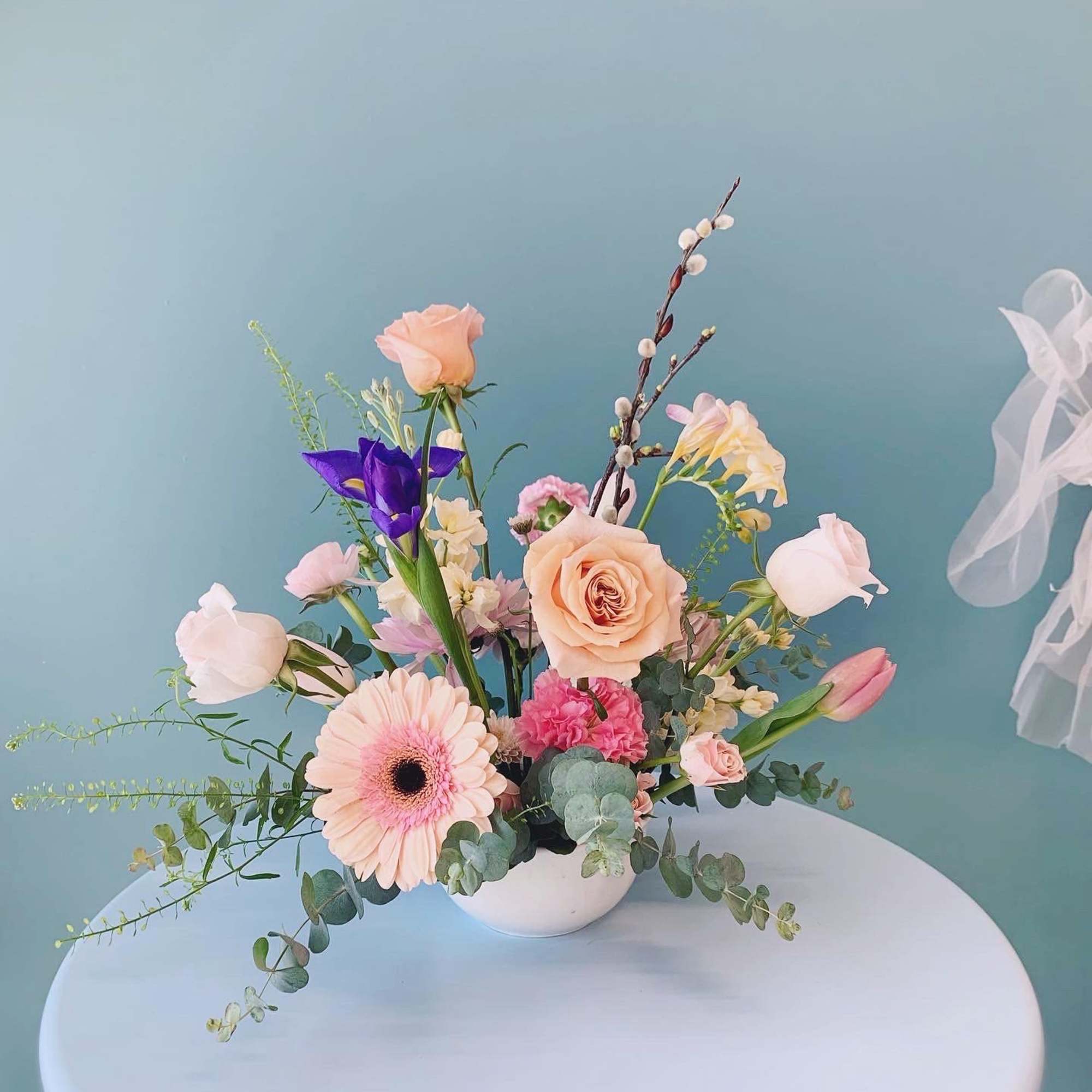 Pastel floral arrangement in a white bowl vase with roses, gerbera daisy, and tulips