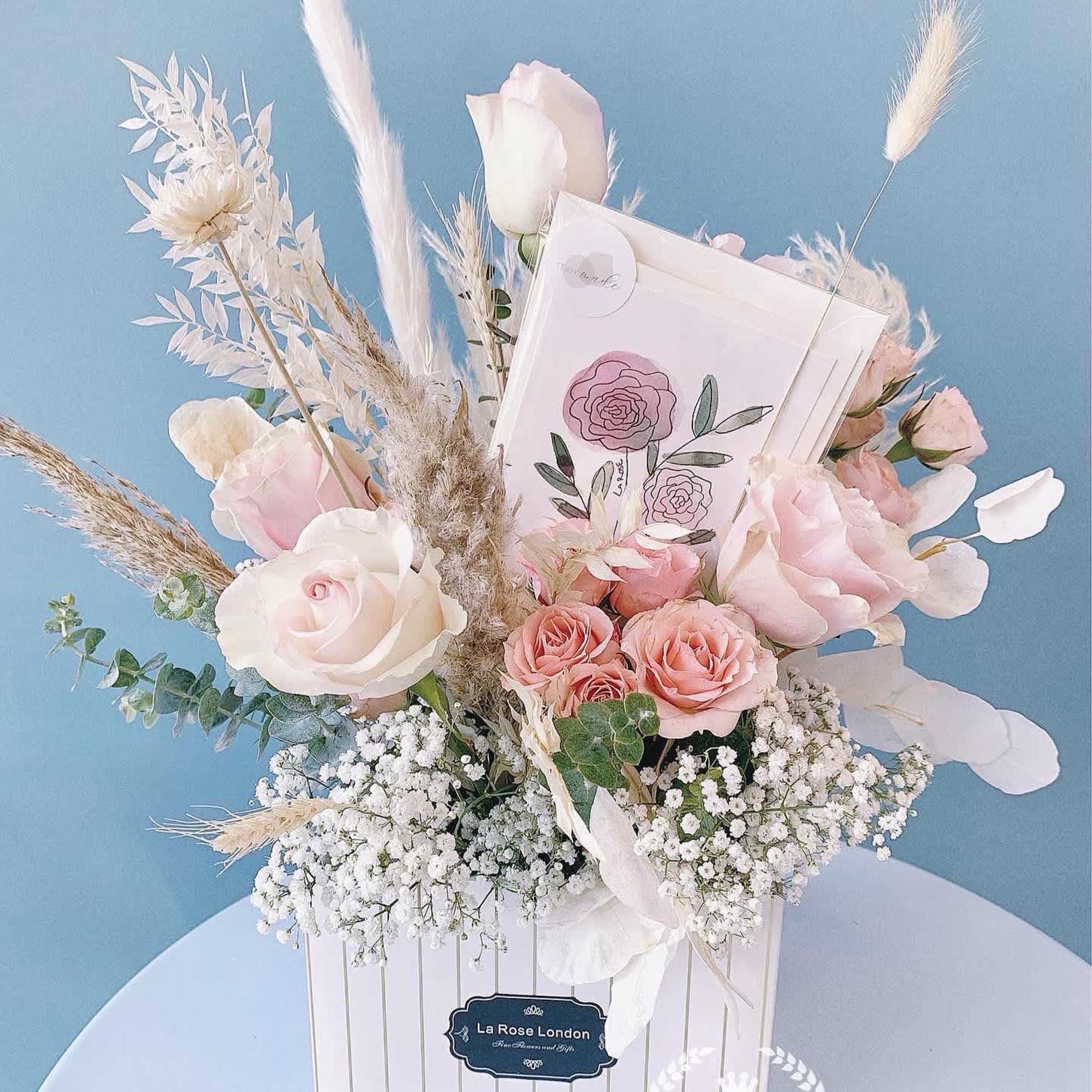 Pastel pink and white roses in a white gift box with dried grasses