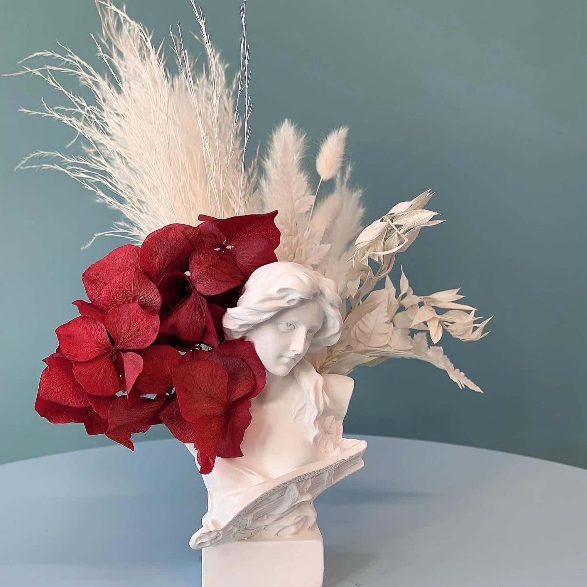 Red hydrangea arrangement in a white bust vase with dried white accents