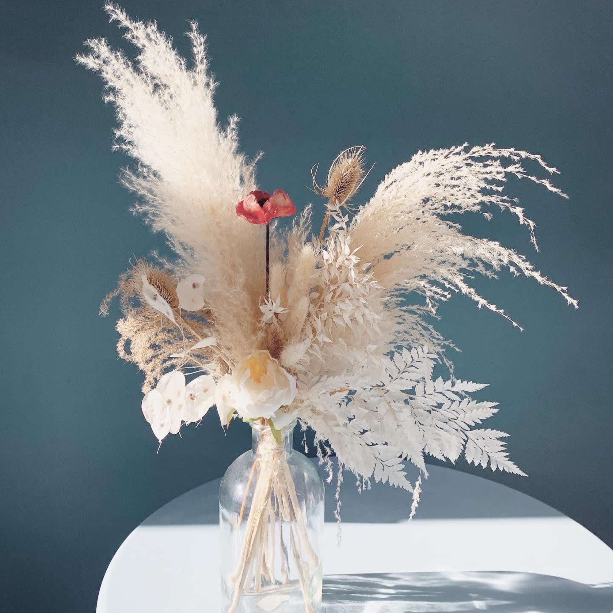 Dried floral arrangement in a clear glass vase with white feathery plumes and small red accents