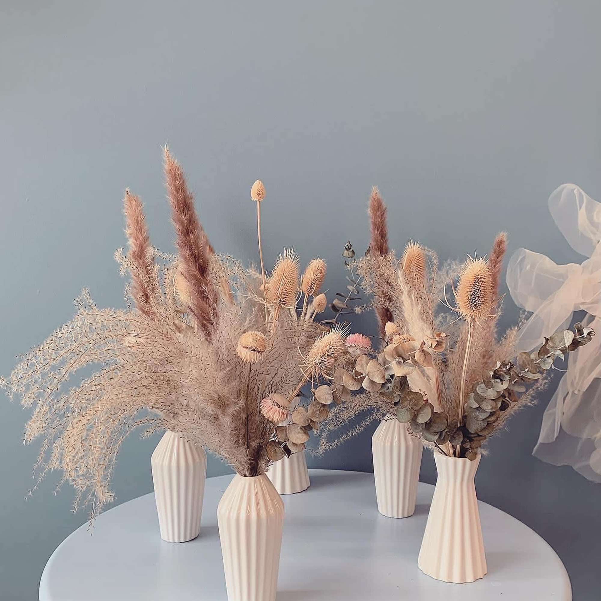 Dried floral arrangements in cream vases on a round table