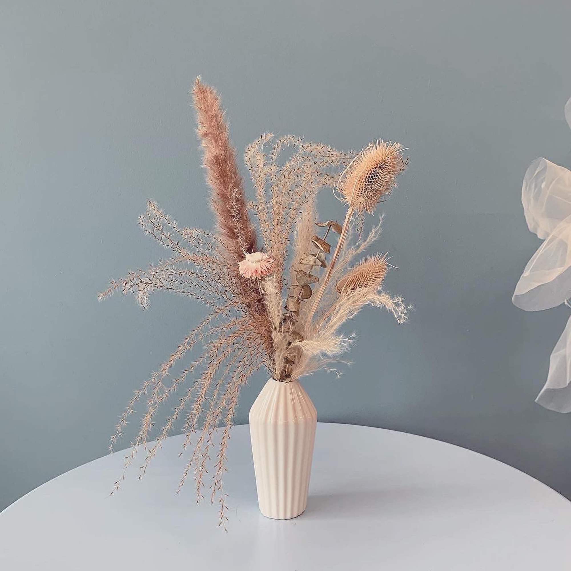 Dried floral arrangement in a white vase with feathery stems