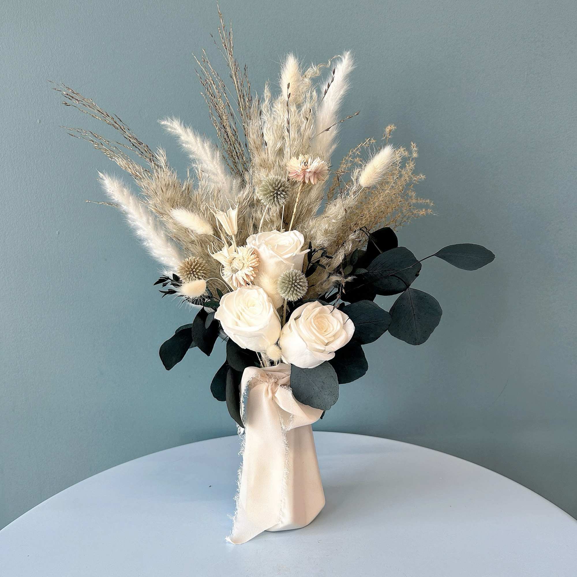 Bouquet of white roses and dried grasses in a wrapped vase