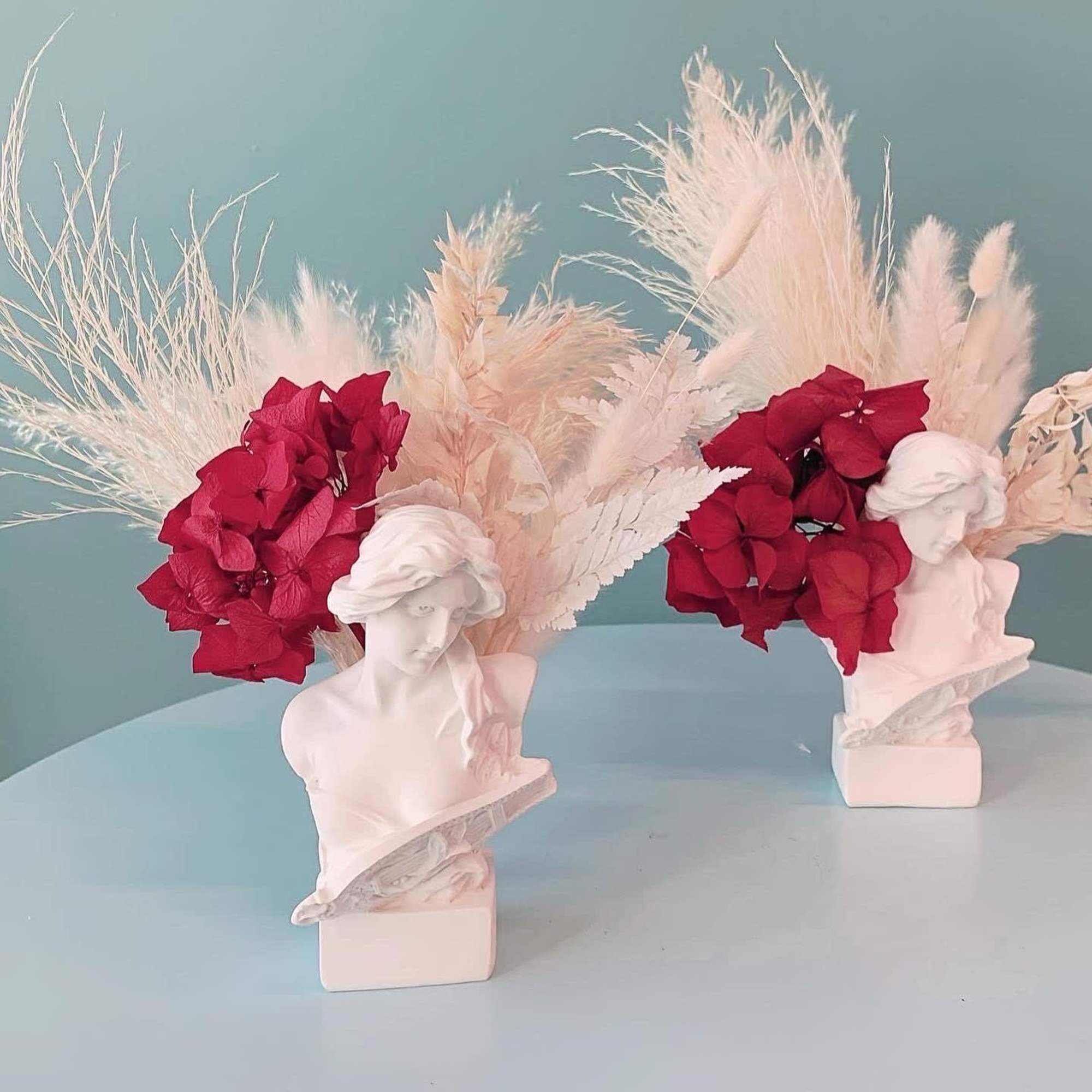 Two floral bust sculptures with red hydrangeas and pale dried plumes
