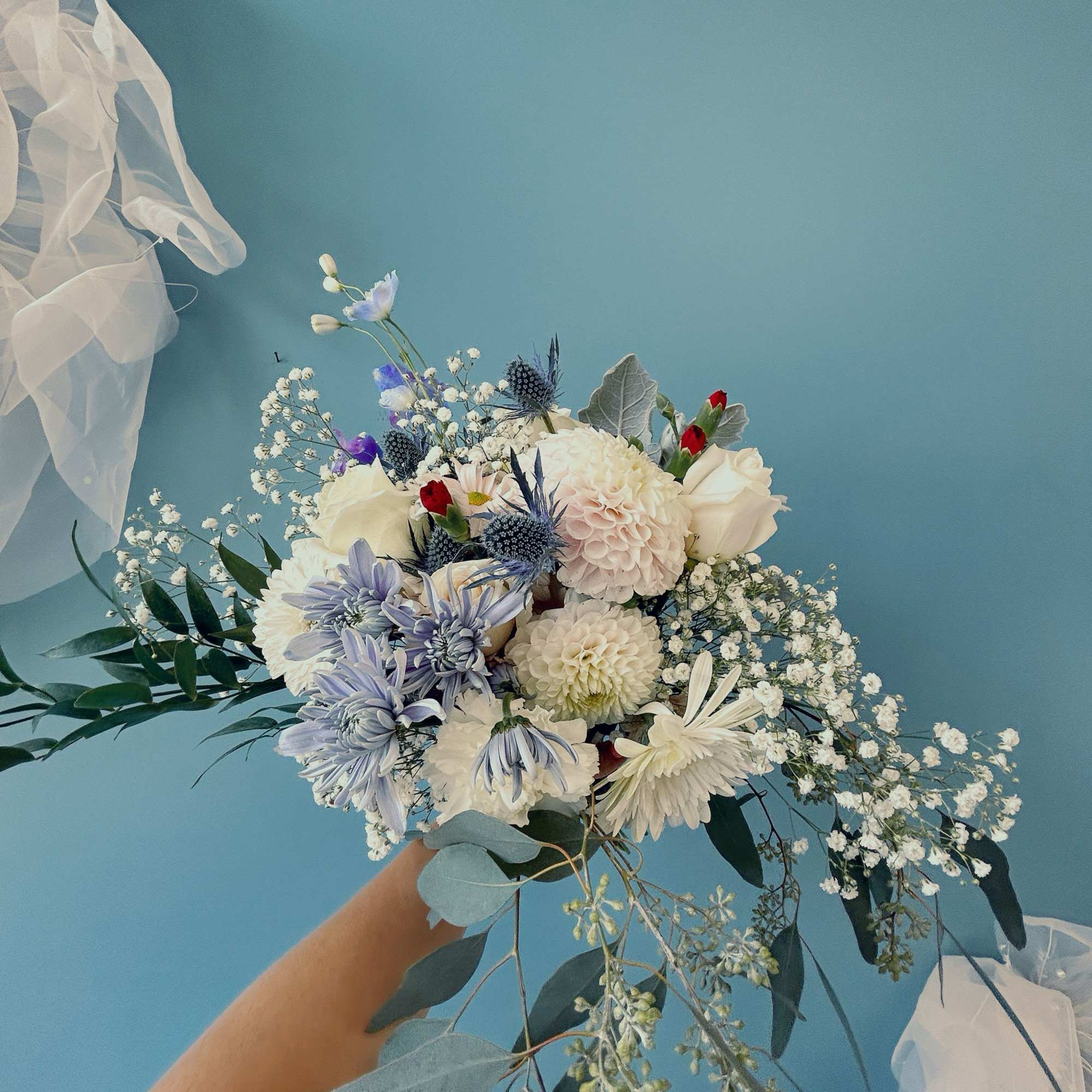 Handheld bouquet of white and pale blue flowers with trailing greenery