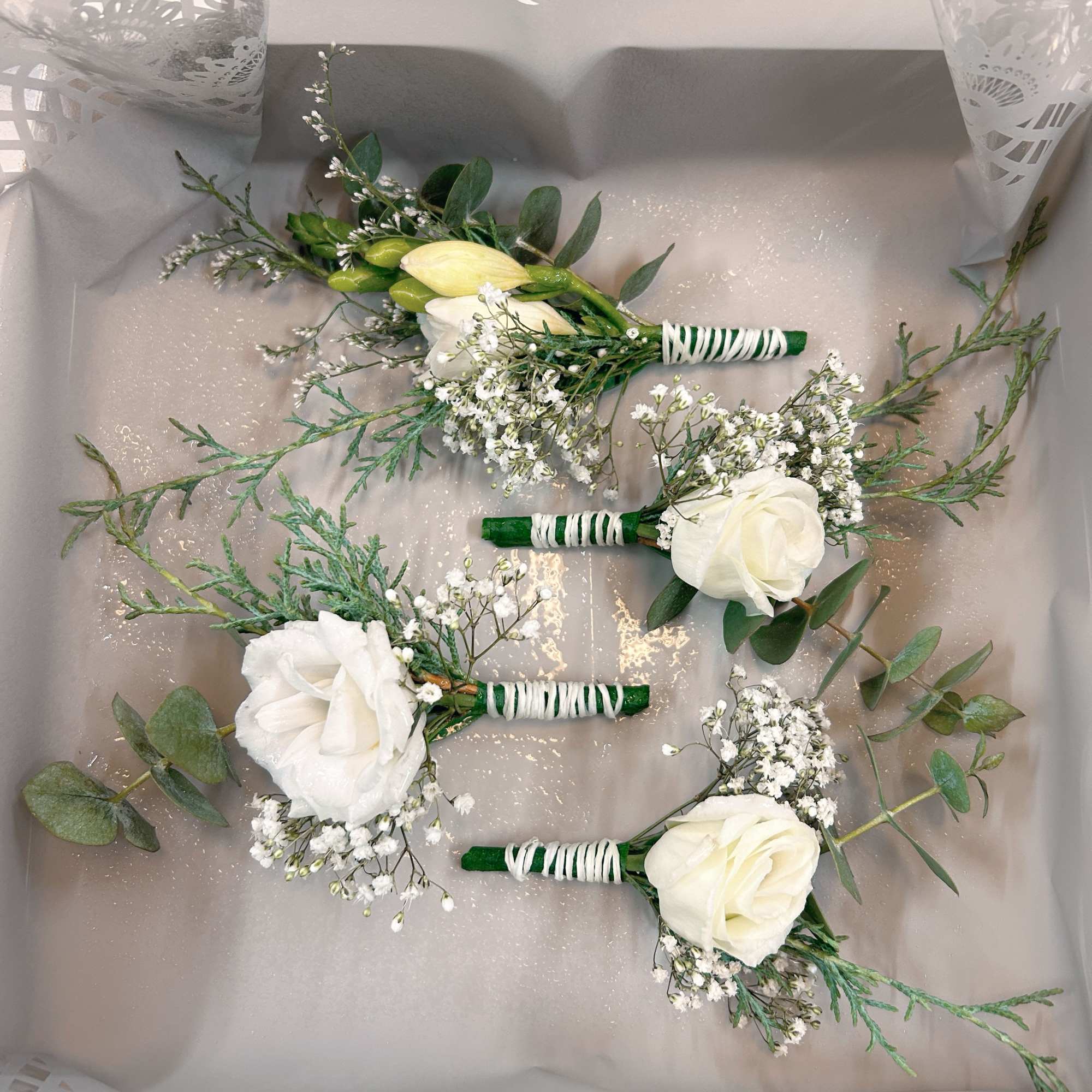 Four white rose boutonnieres with baby's breath and greenery in a gift box