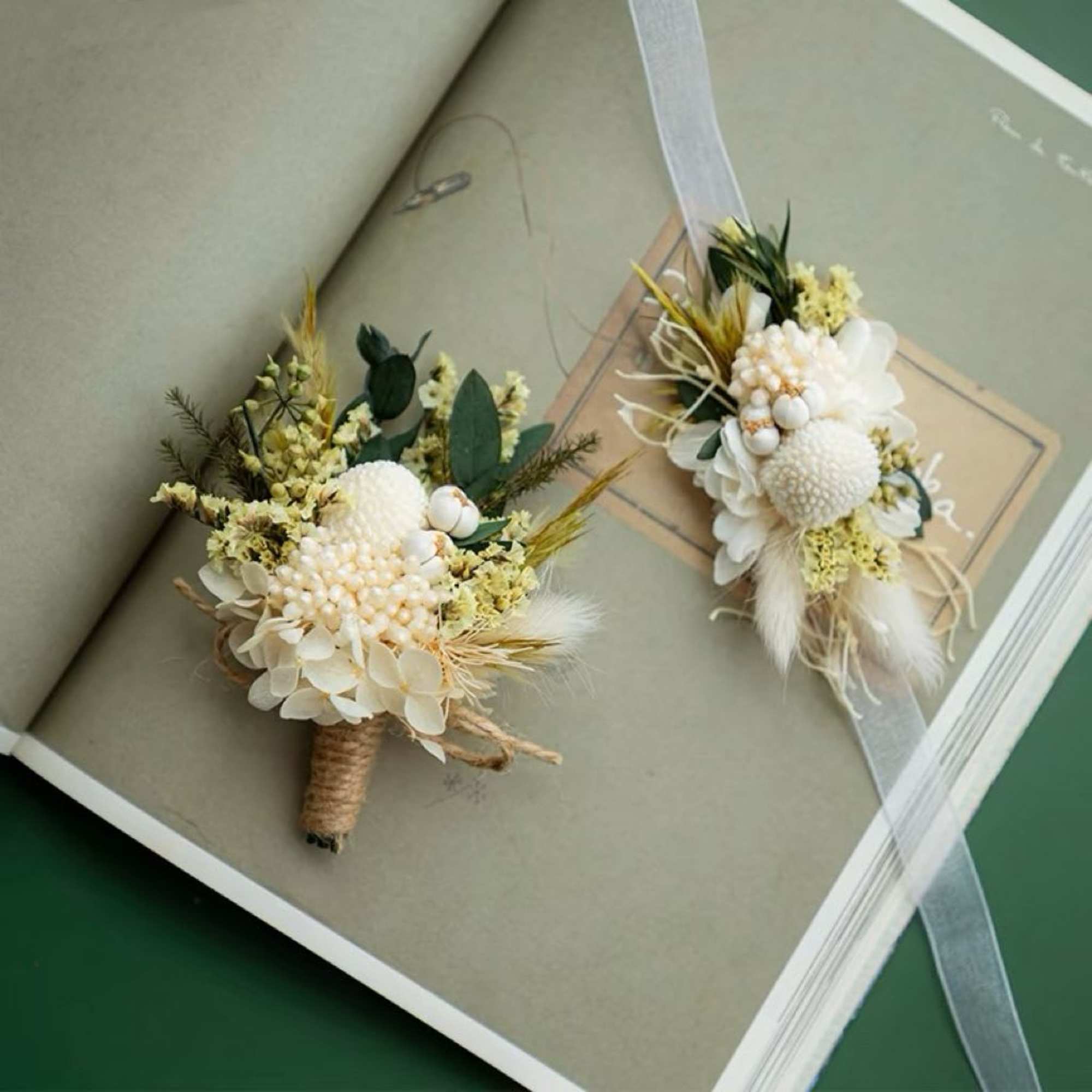 Two small white and cream wedding boutonnieres with ribbon ties