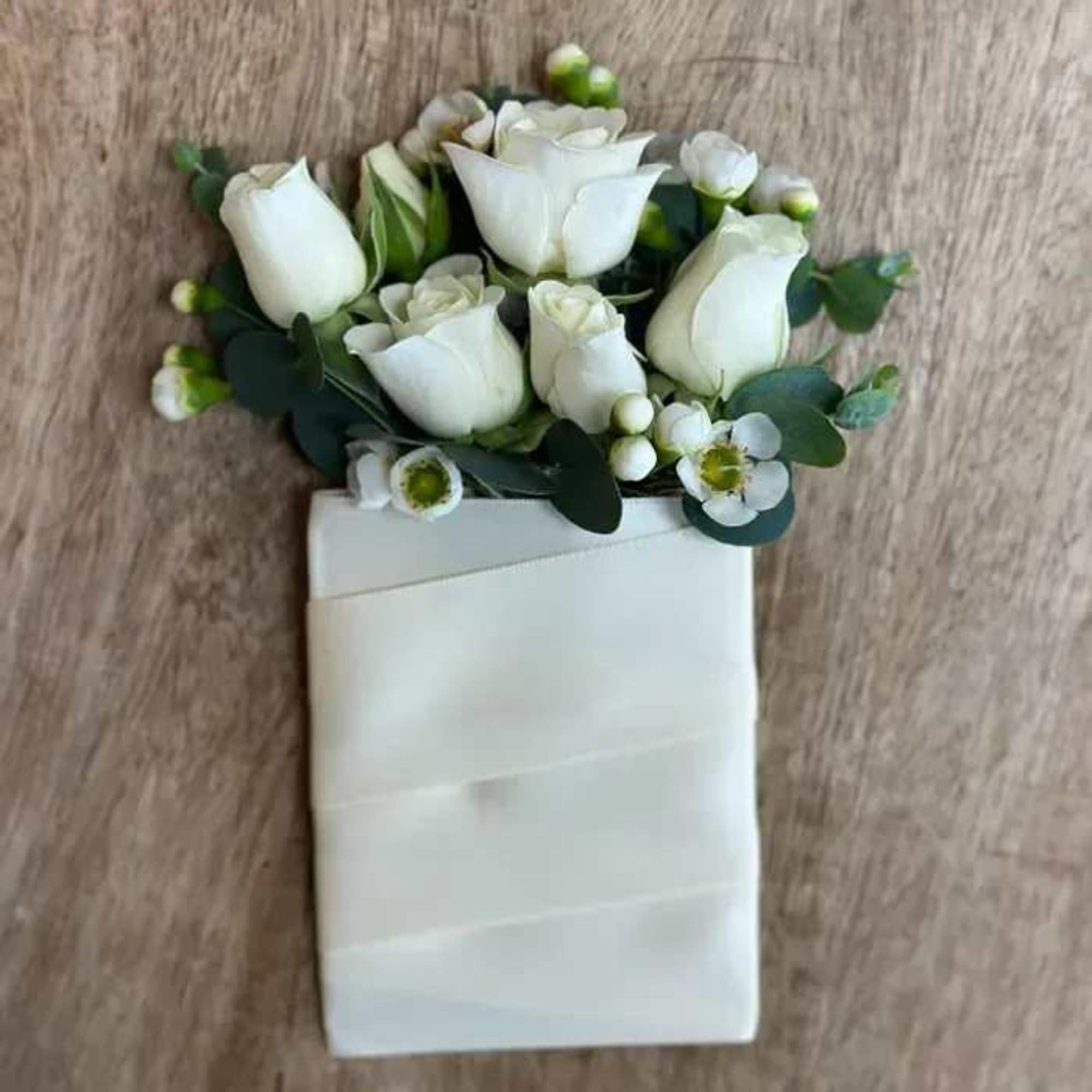 White rose boutonniere with small white blossoms and greenery on a white wrap