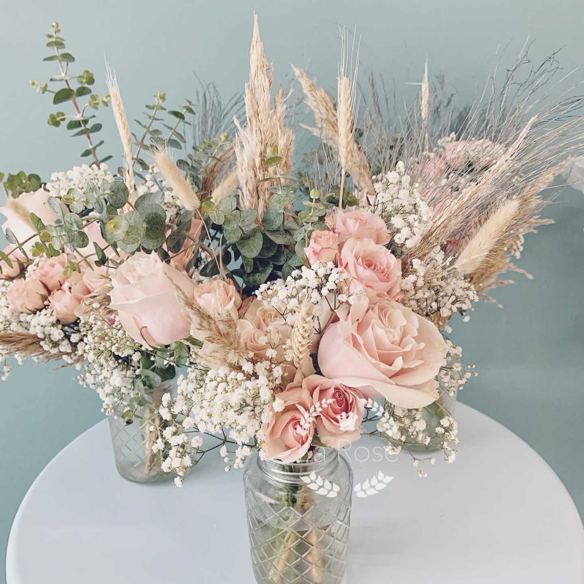 Blush roses and baby's breath in glass jars with dried grasses