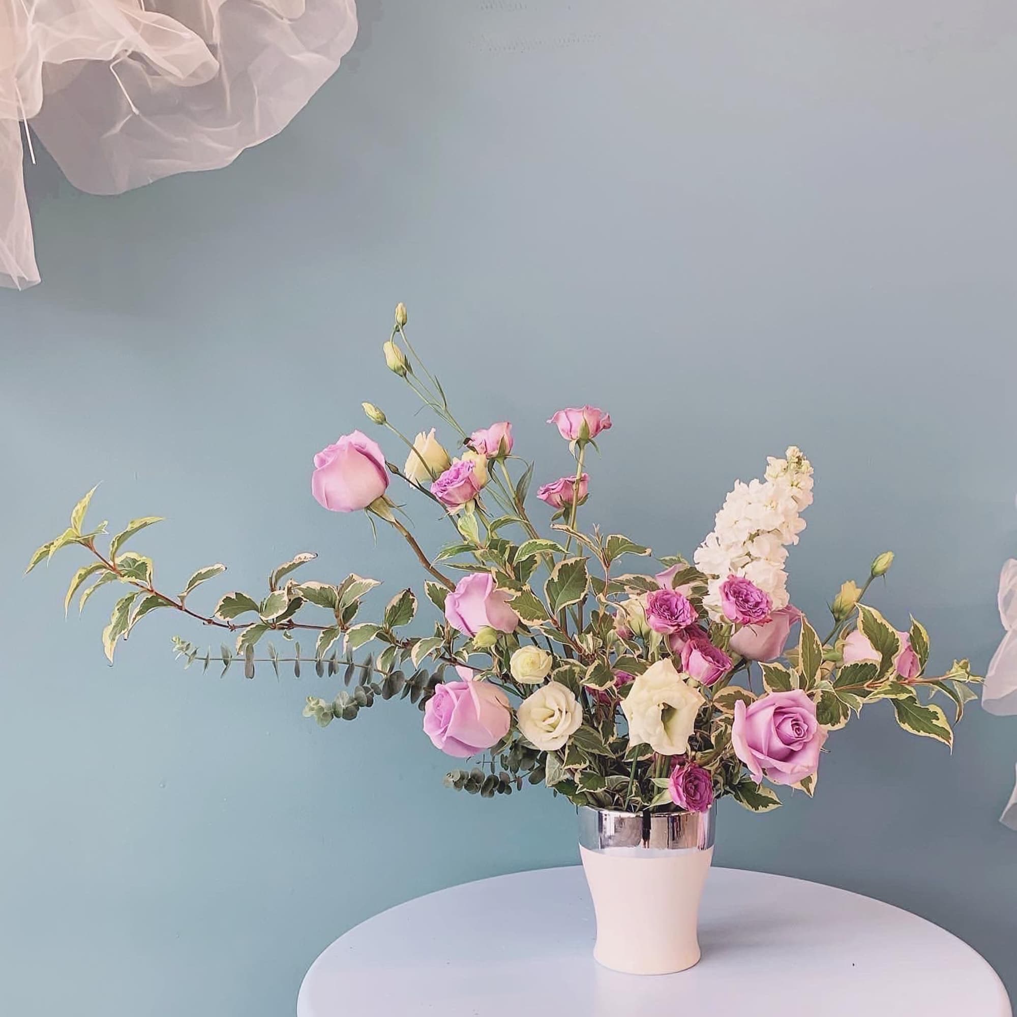 Pink and white roses in a white vase with variegated foliage
