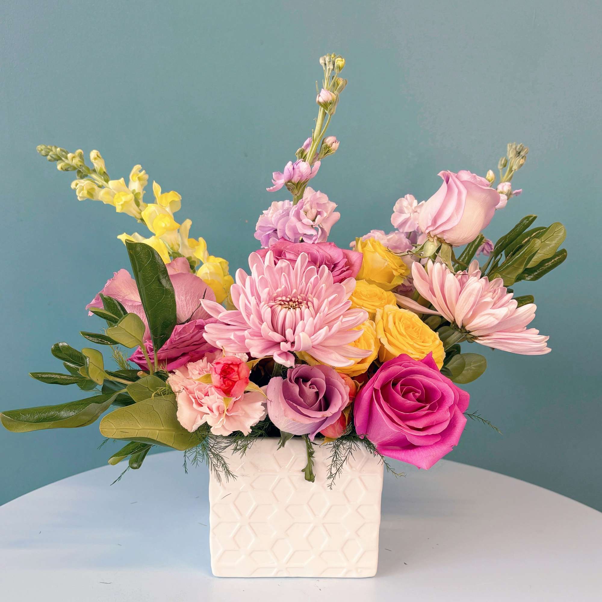 Pink and yellow mixed bouquet in a white square vase