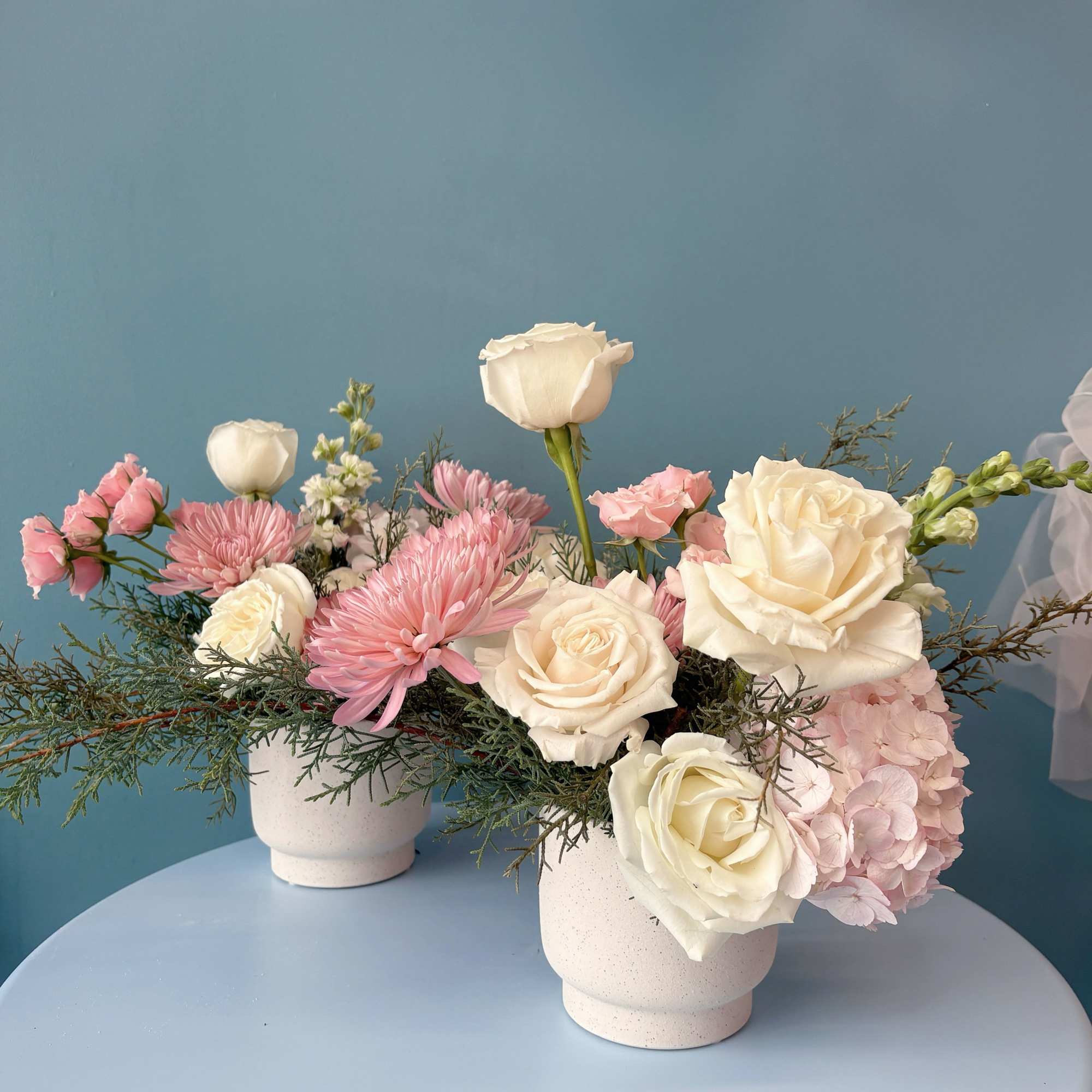 Pink and white floral arrangements in white pots on a round table