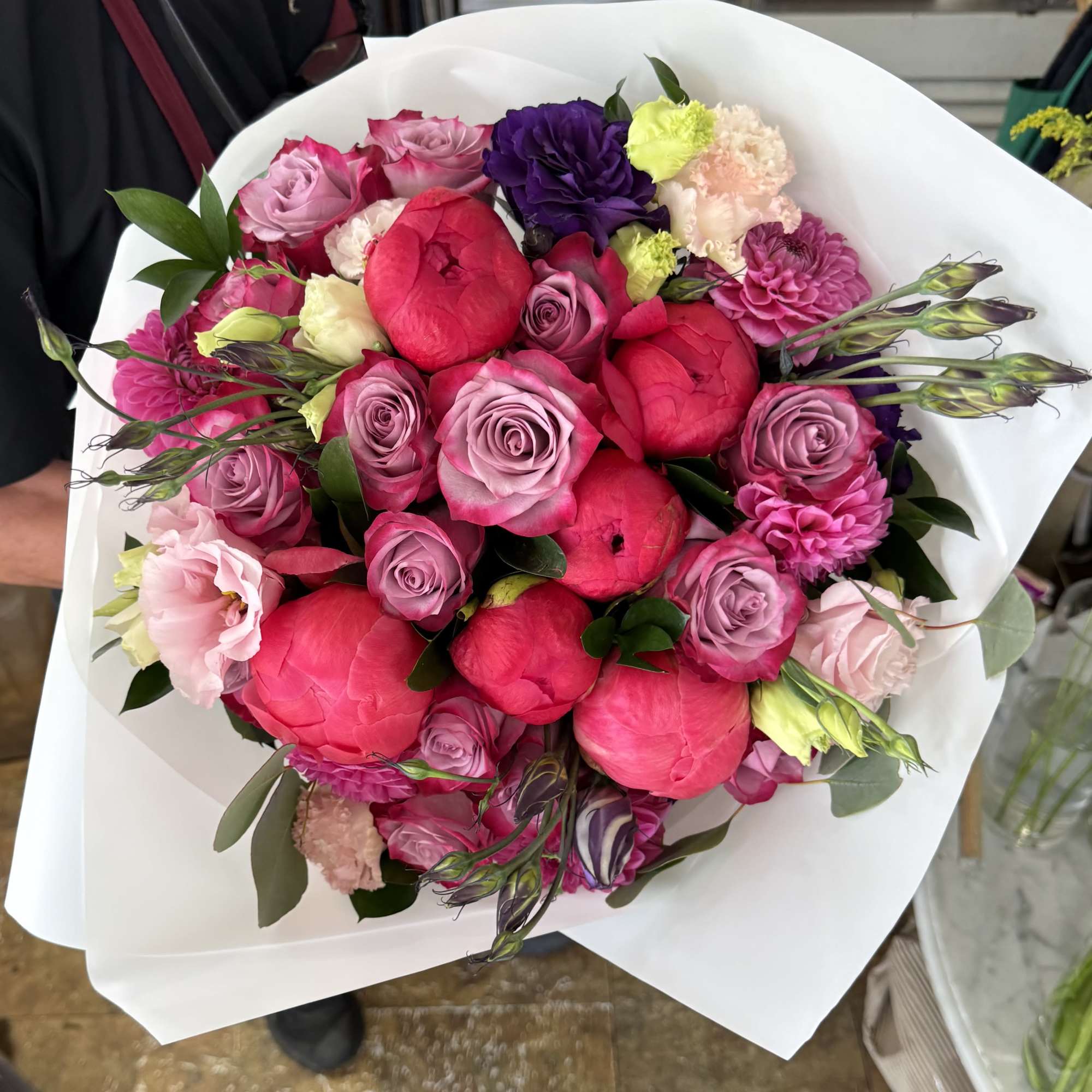 A lavish hand-tied bouquet where vibrant coral peonies meet elegant lavender roses