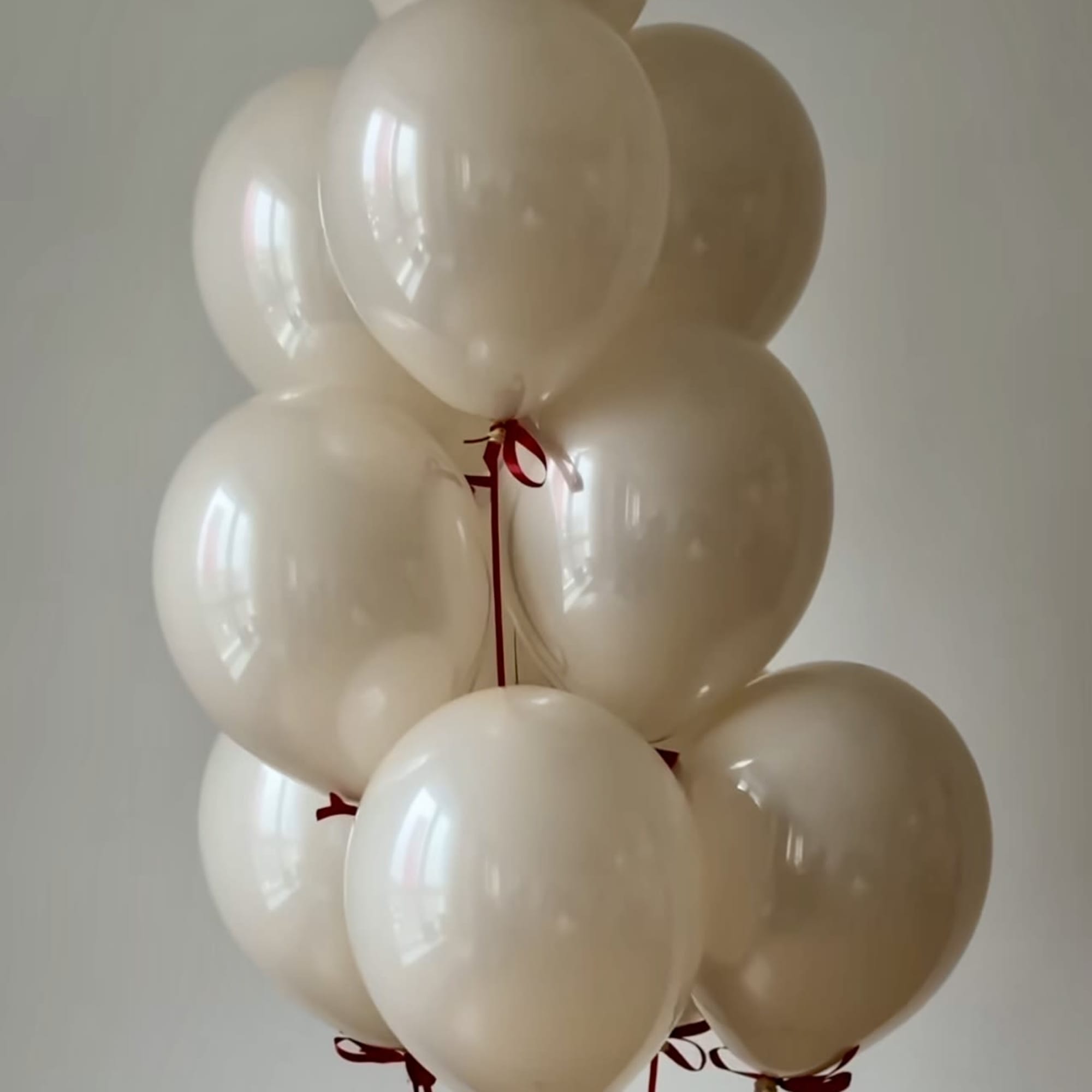 Cluster of cream-colored balloons tied with red ribbons