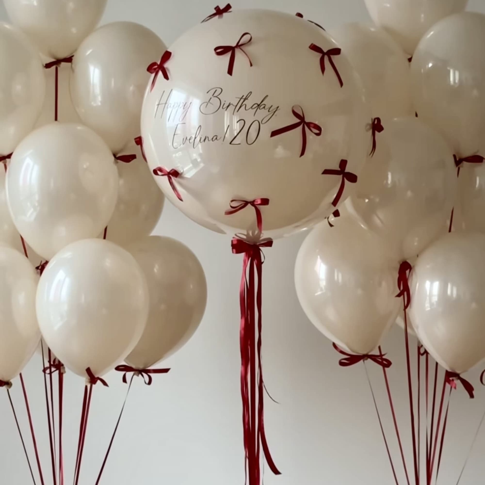 Cream balloons with red ribbons, including a personalized birthday balloon