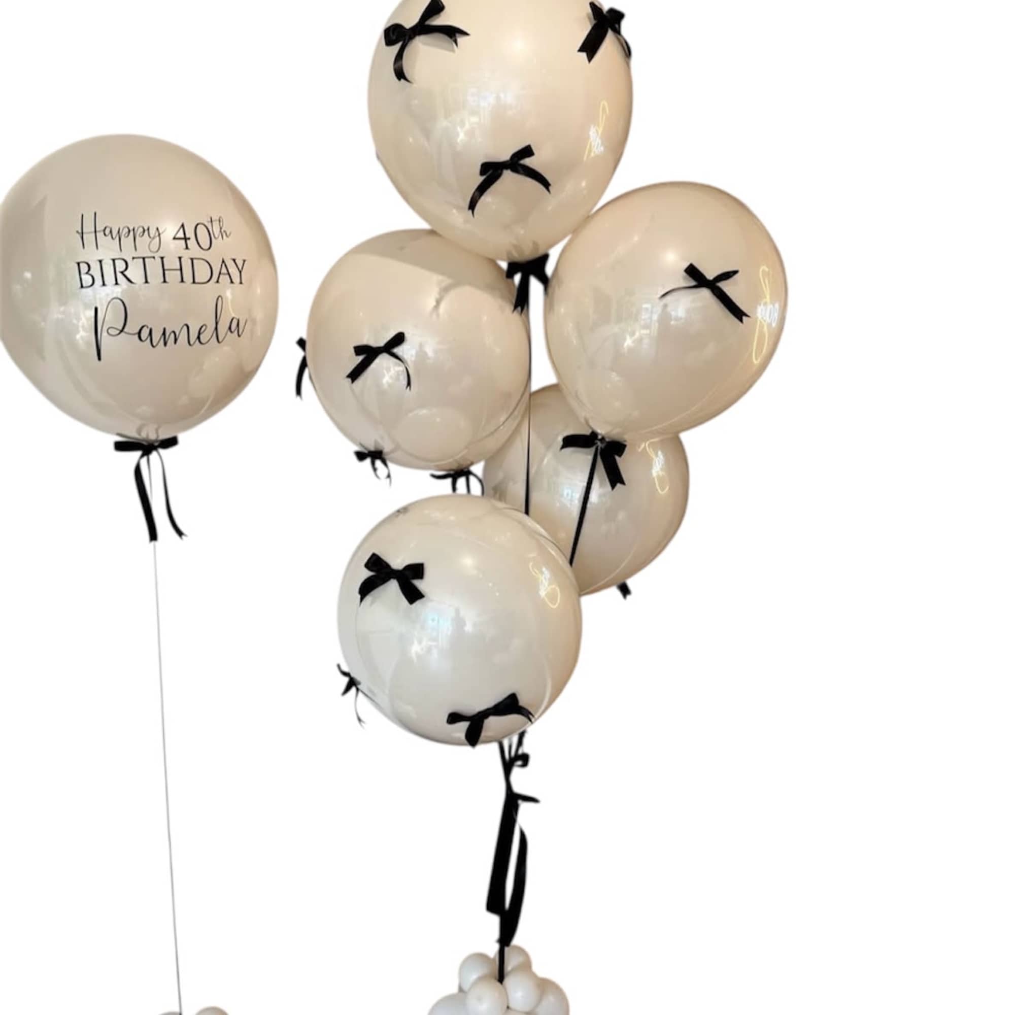 Cream birthday balloons with black bows and one personalized balloon.