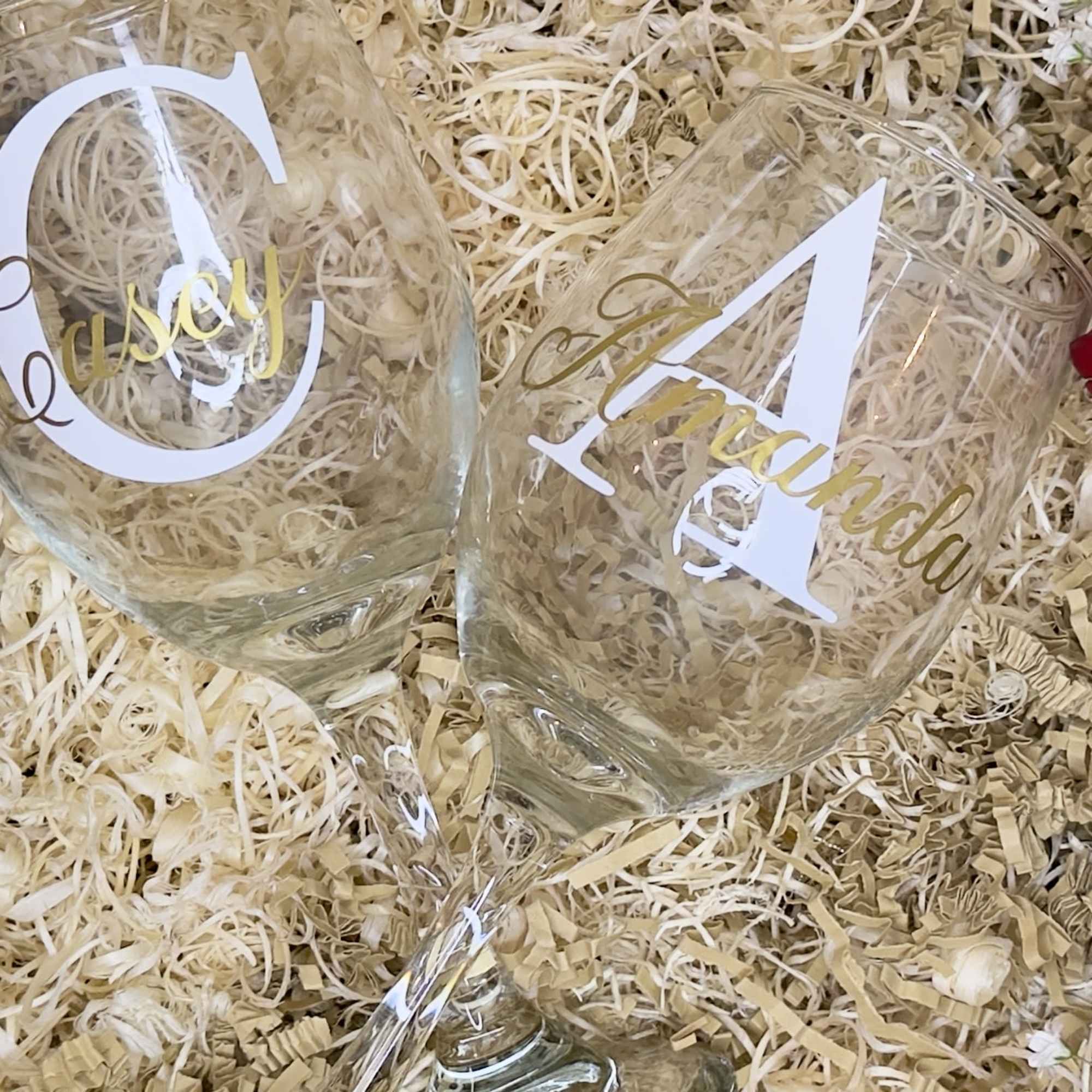 Two engraved wine glasses resting in shredded filler