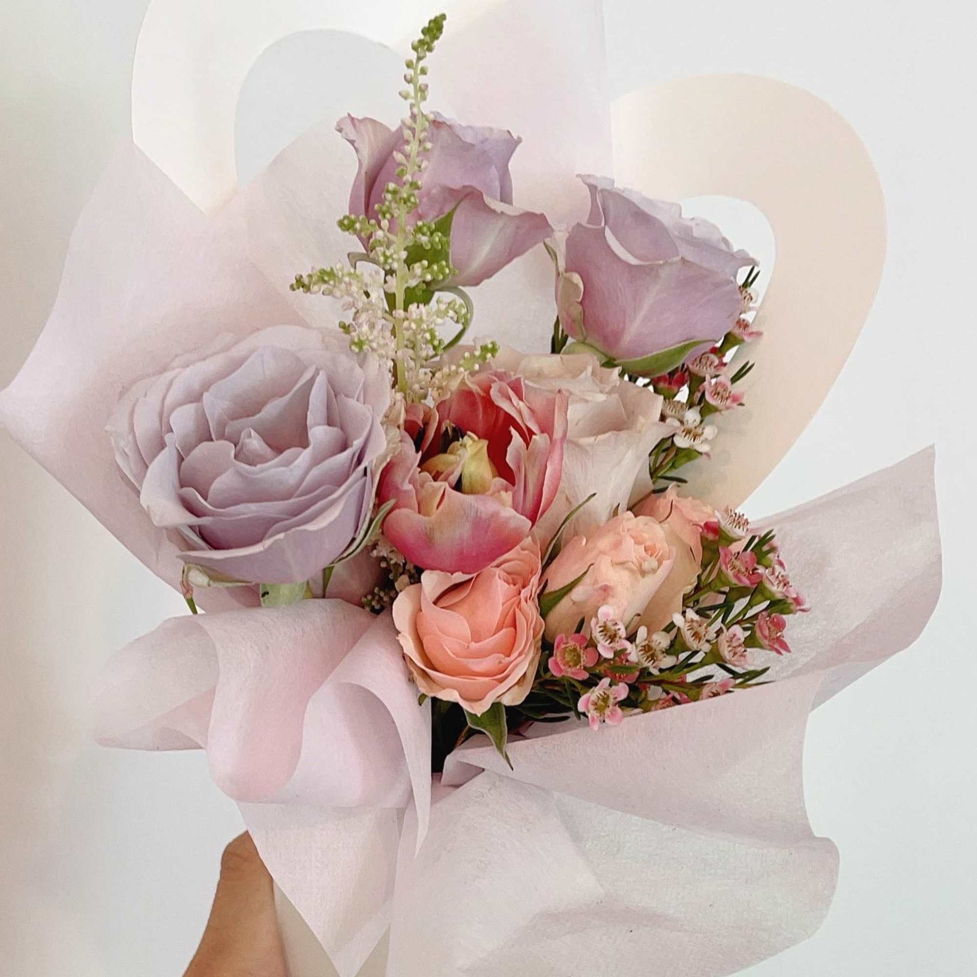 Handheld bouquet of pastel roses and tulips wrapped in pale pink paper