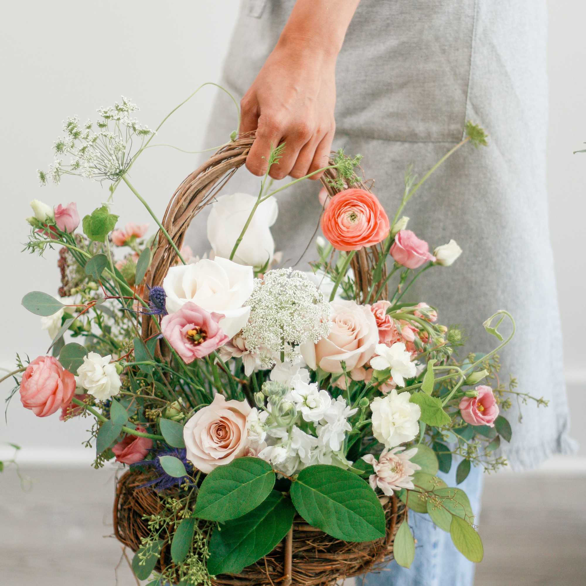 Person holding a wicker basket filled with pastel flowers