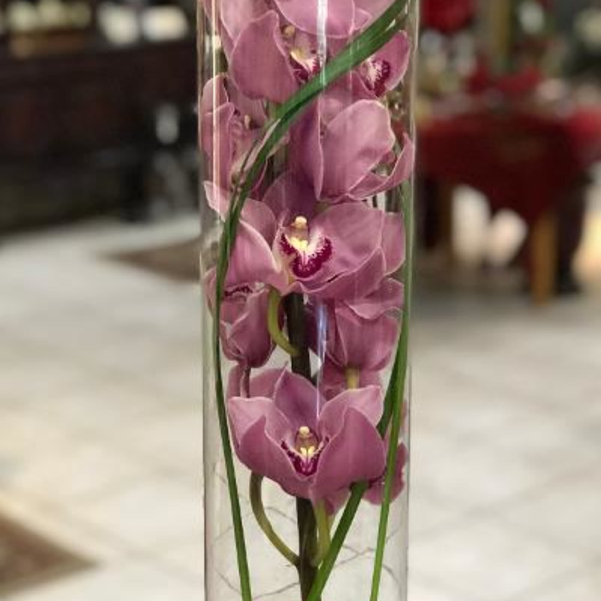 Pink orchids arranged in a tall clear cylinder vase with a ribbon bow