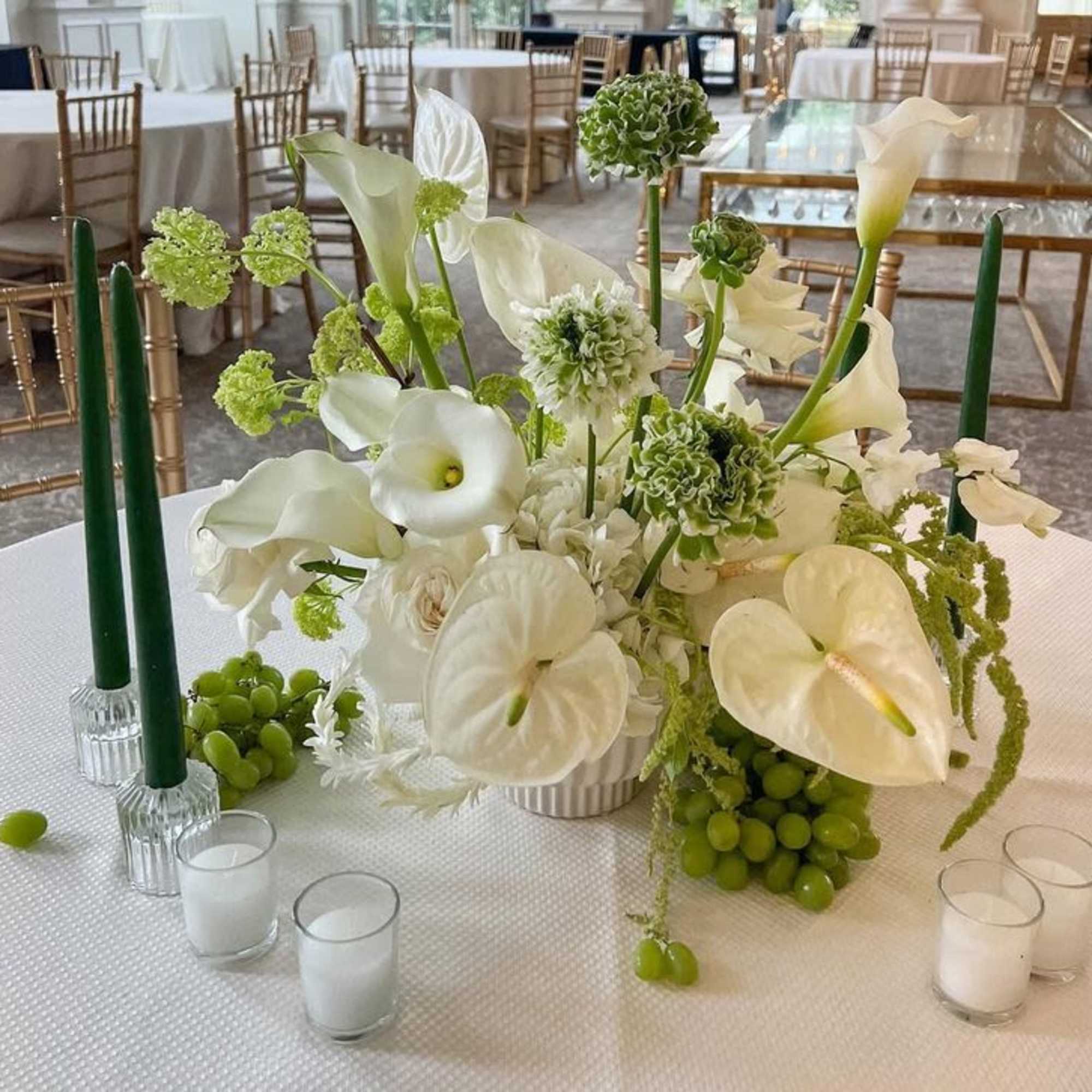 A low, lush wedding centerpiece built around sculptural white anthuriums, calla lilies