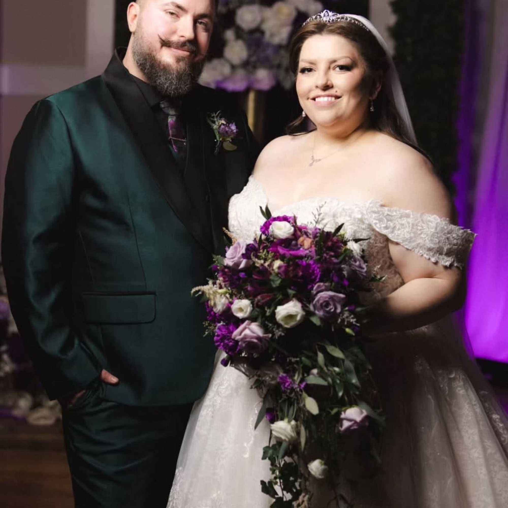 Bride holding a cascading purple and white bouquet beside the groom