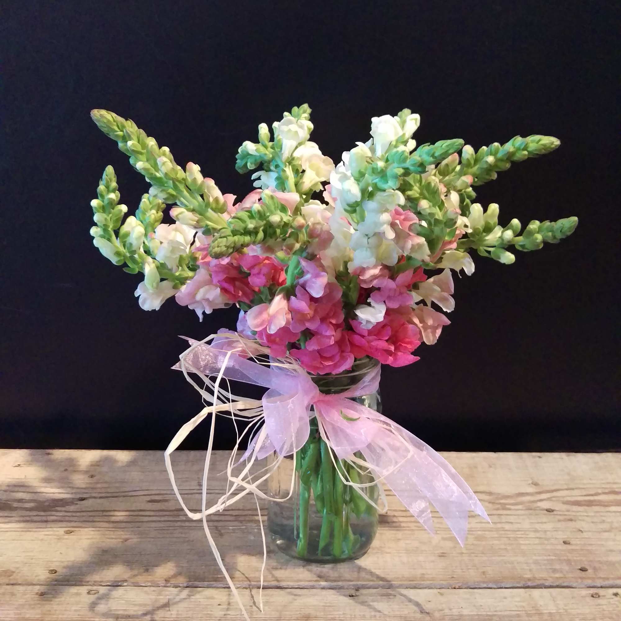 Pink and white flowers in a glass vase with a ribbon bow