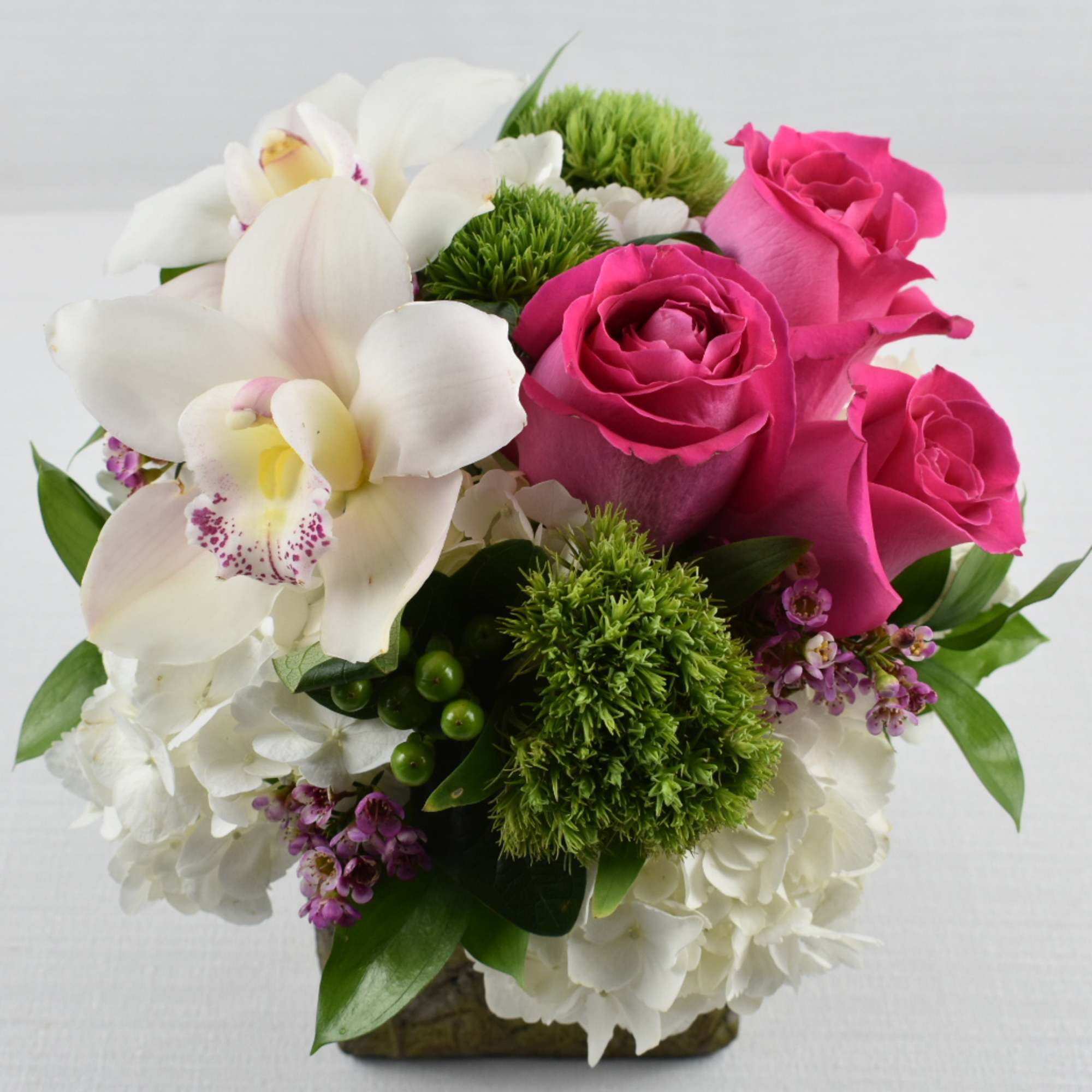 Compact arrangement of hot pink roses, white orchids, and hydrangeas in a square vase