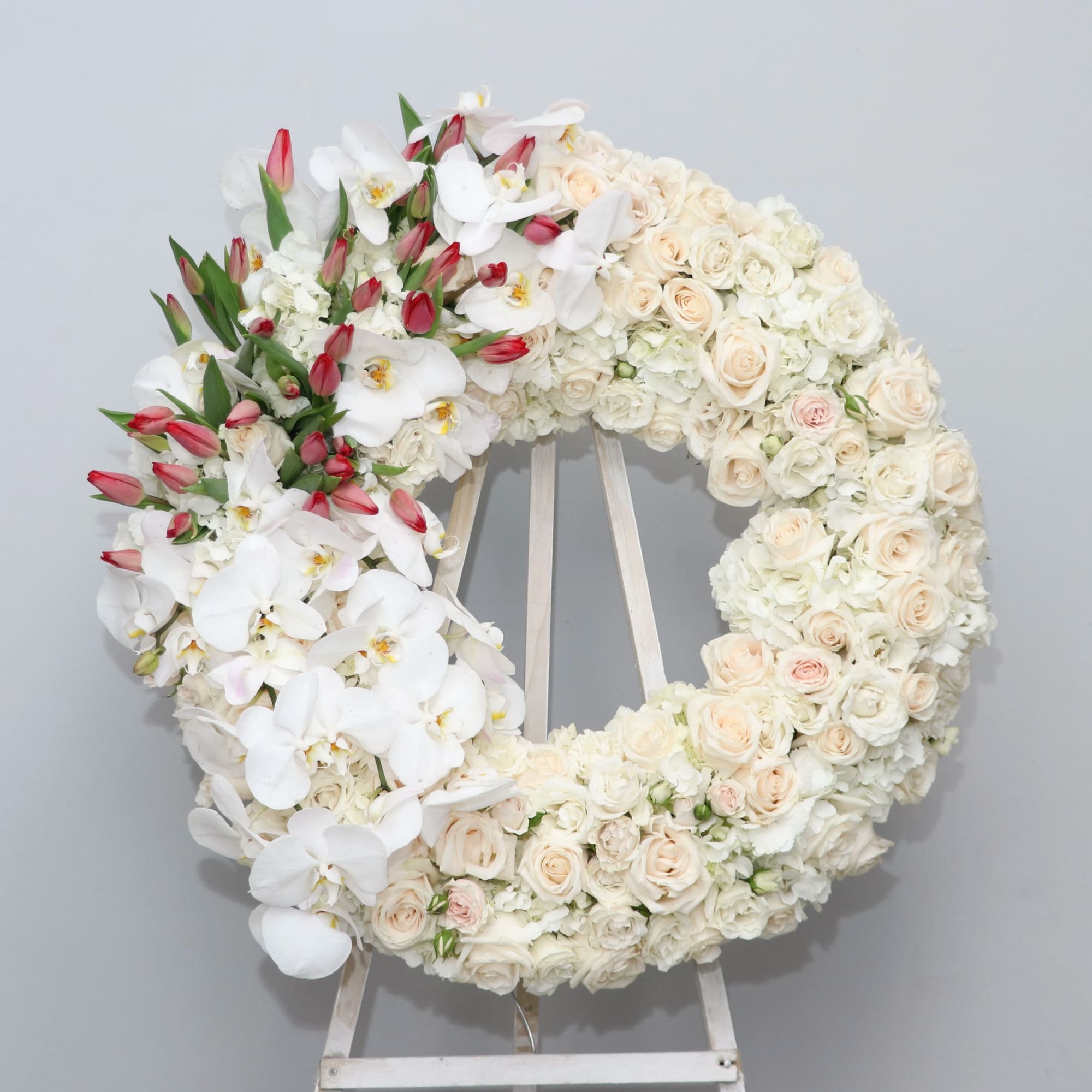 Large white floral wreath with pale roses and orchids on an easel