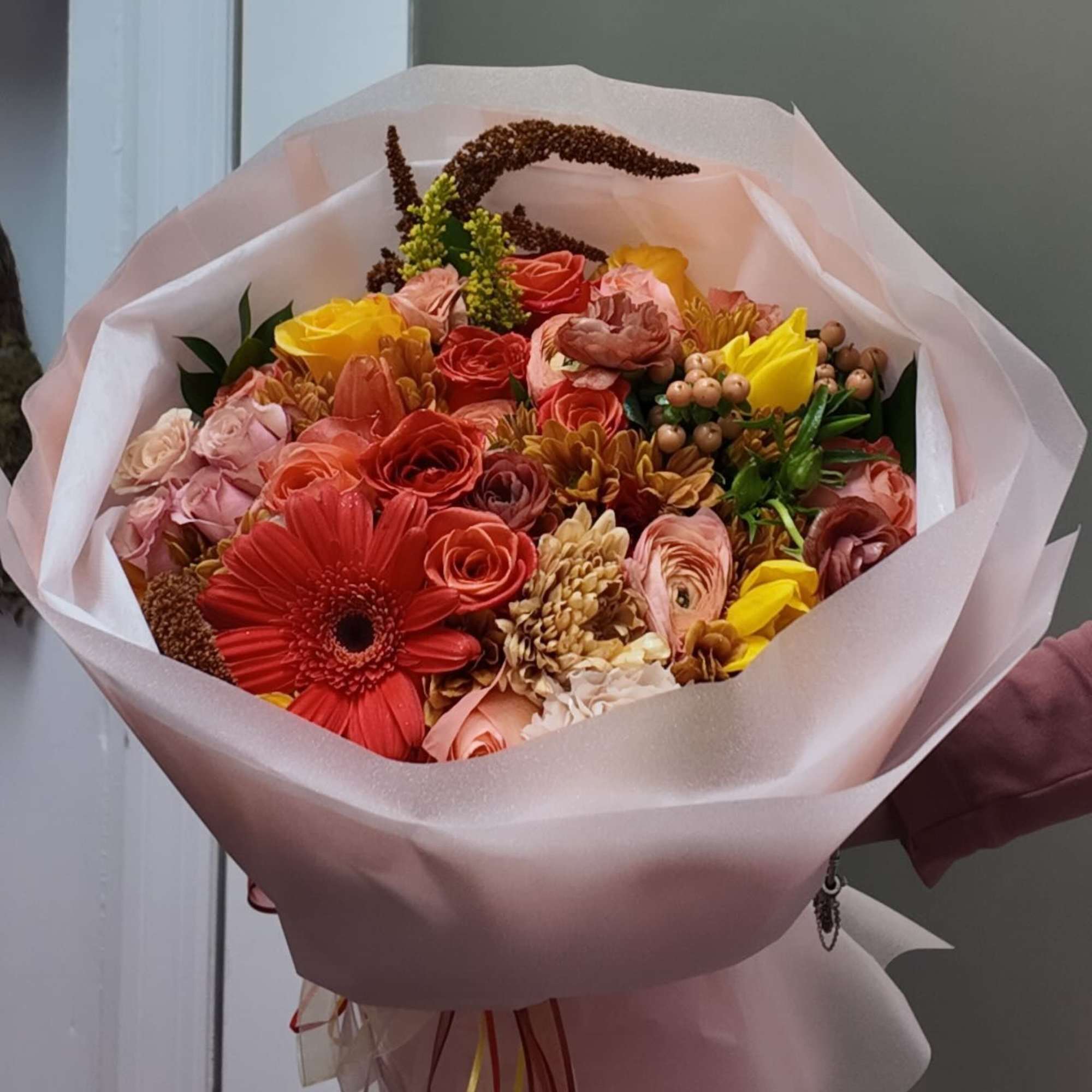 Bouquet of red, pink, and yellow flowers wrapped in pale pink paper